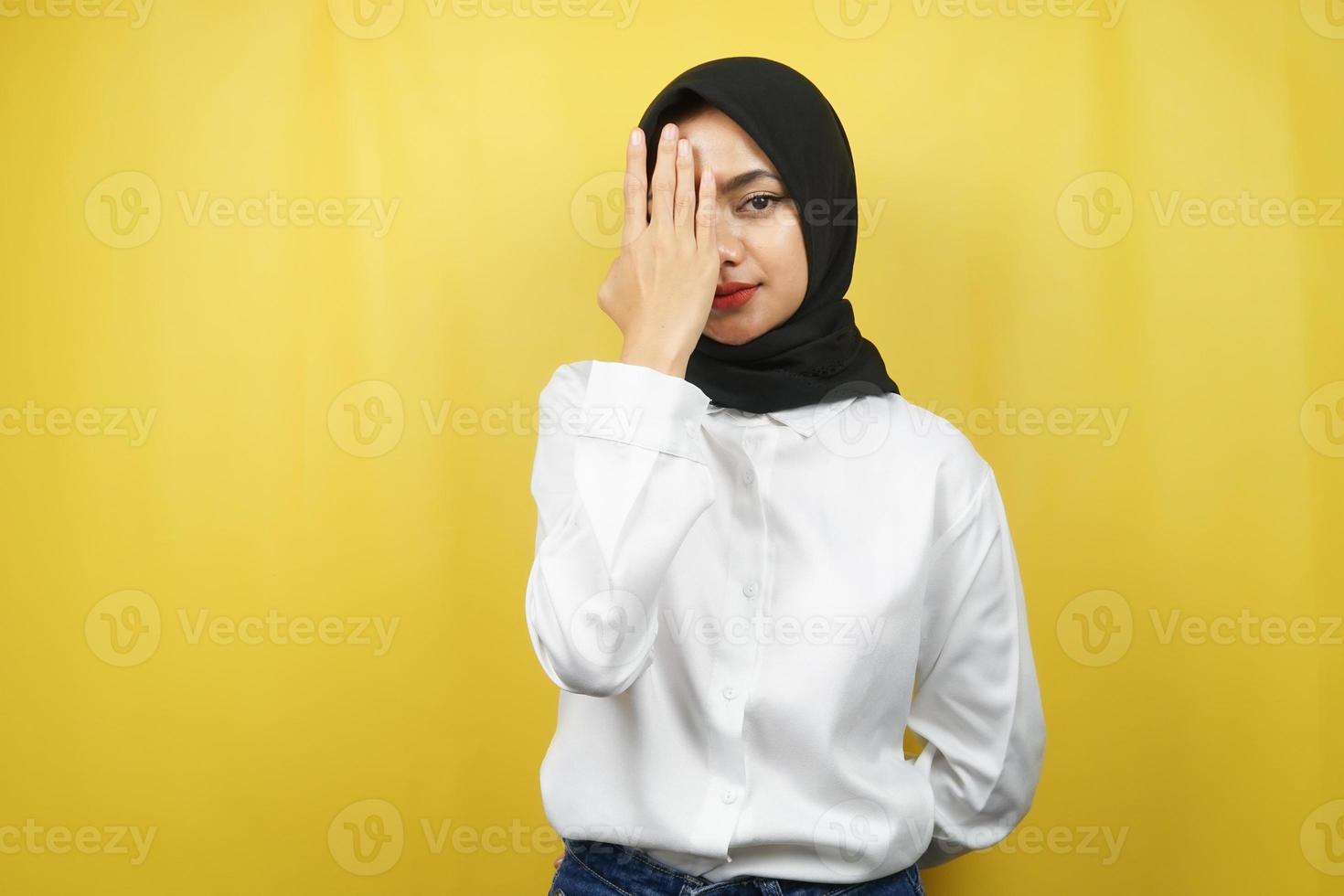 linda jovem muçulmana asiática com a mão cobrindo um olho, olhando para a câmera, isolada no fundo amarelo foto