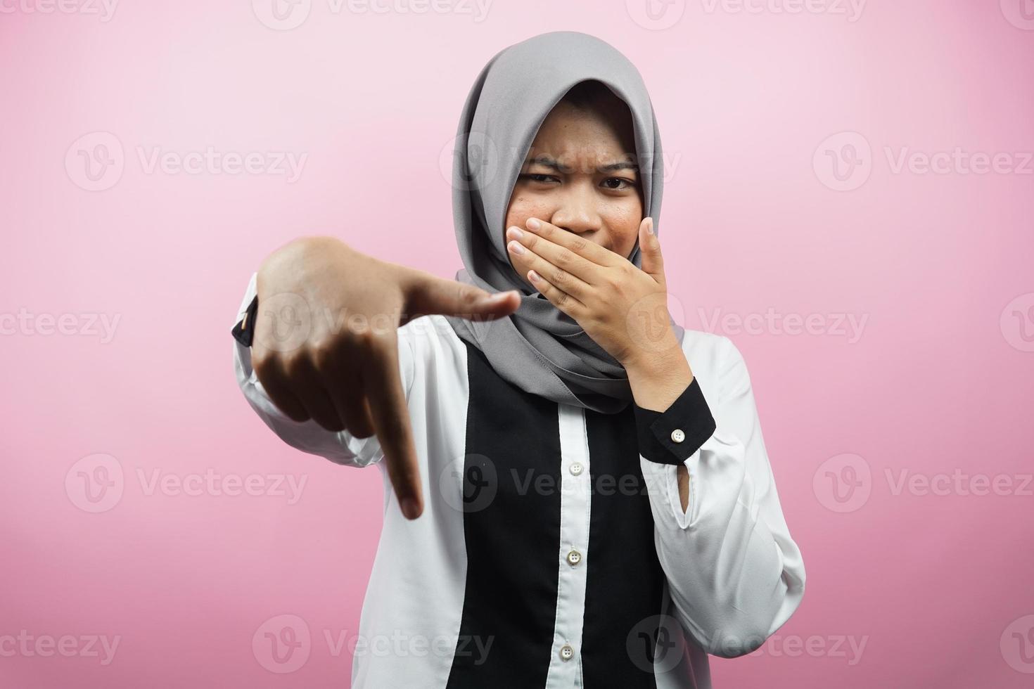 bela jovem muçulmana com a mão cobrindo a boca, a mão apontando para baixo, mostrando expressão de desaprovação, mostrando repulsa por algo, isolado em um fundo rosa foto