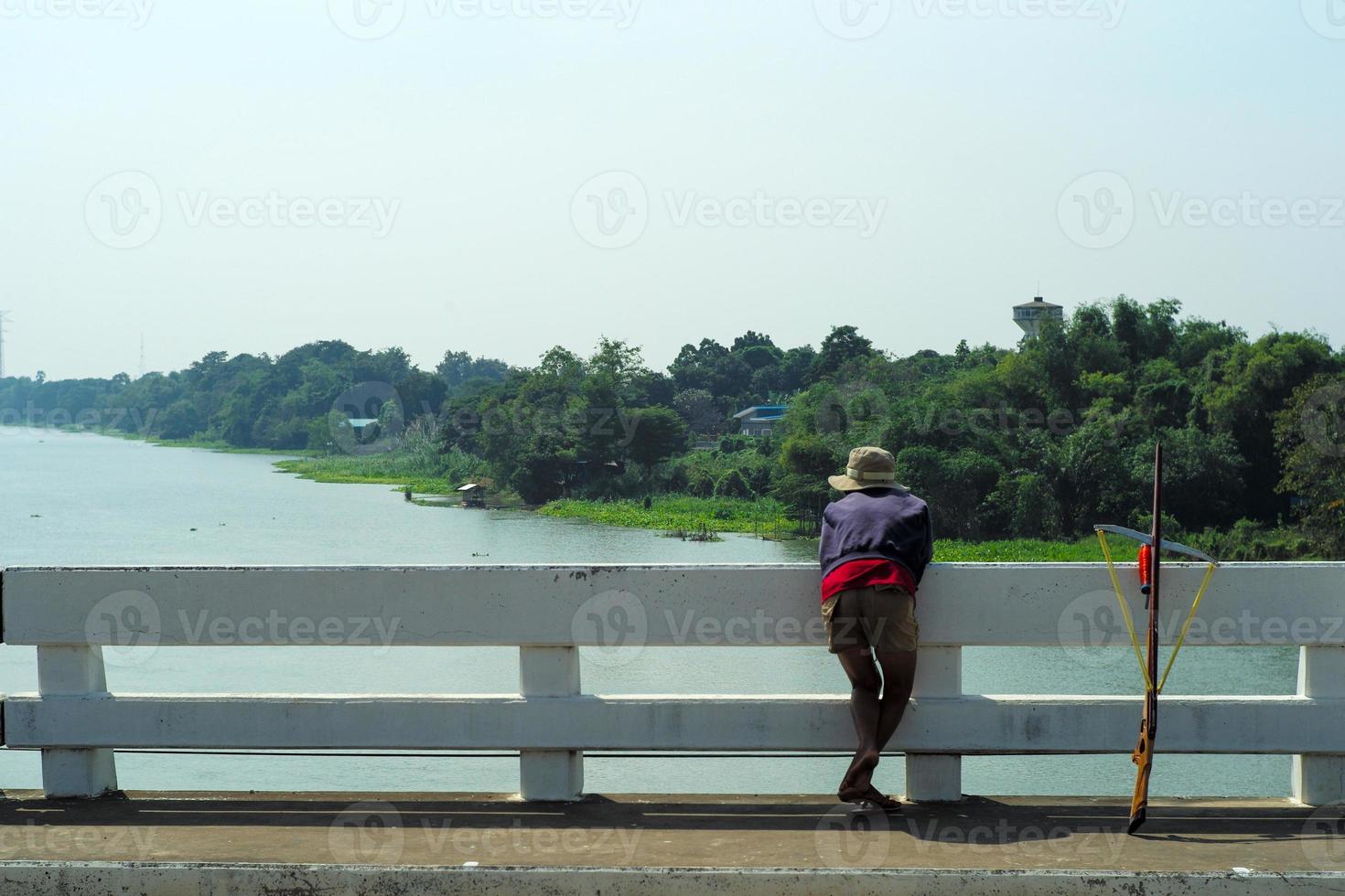 vista traseira do homem procura os peixes no rio para pescar com a arma de madeira com paisagem em bakground foto