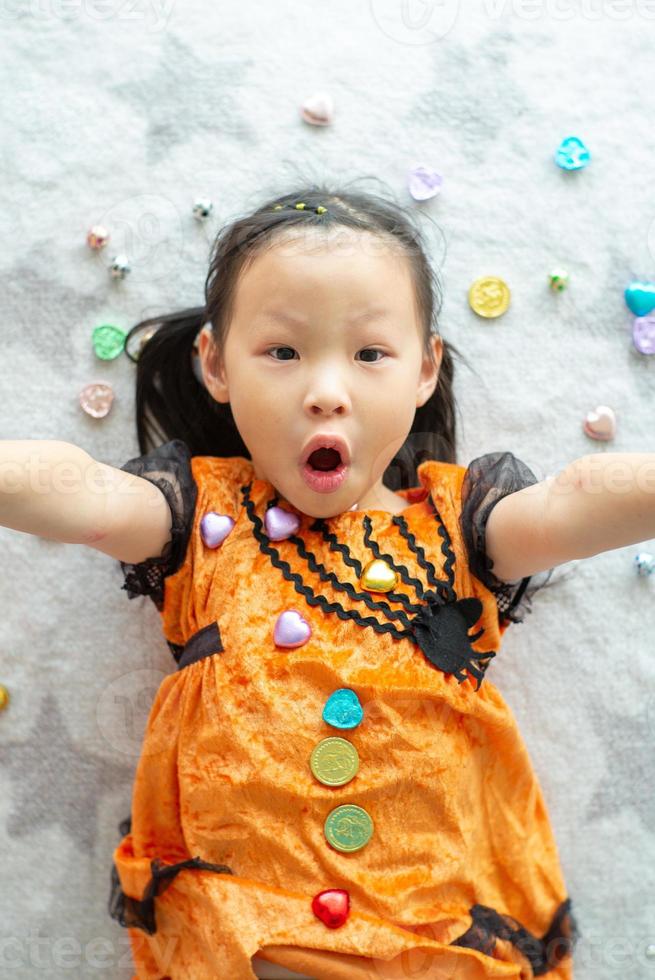 retrato de menina asiática jogando e comendo doces e chocolate de doces ou travessuras com o tema do dia das bruxas em segundo plano foto