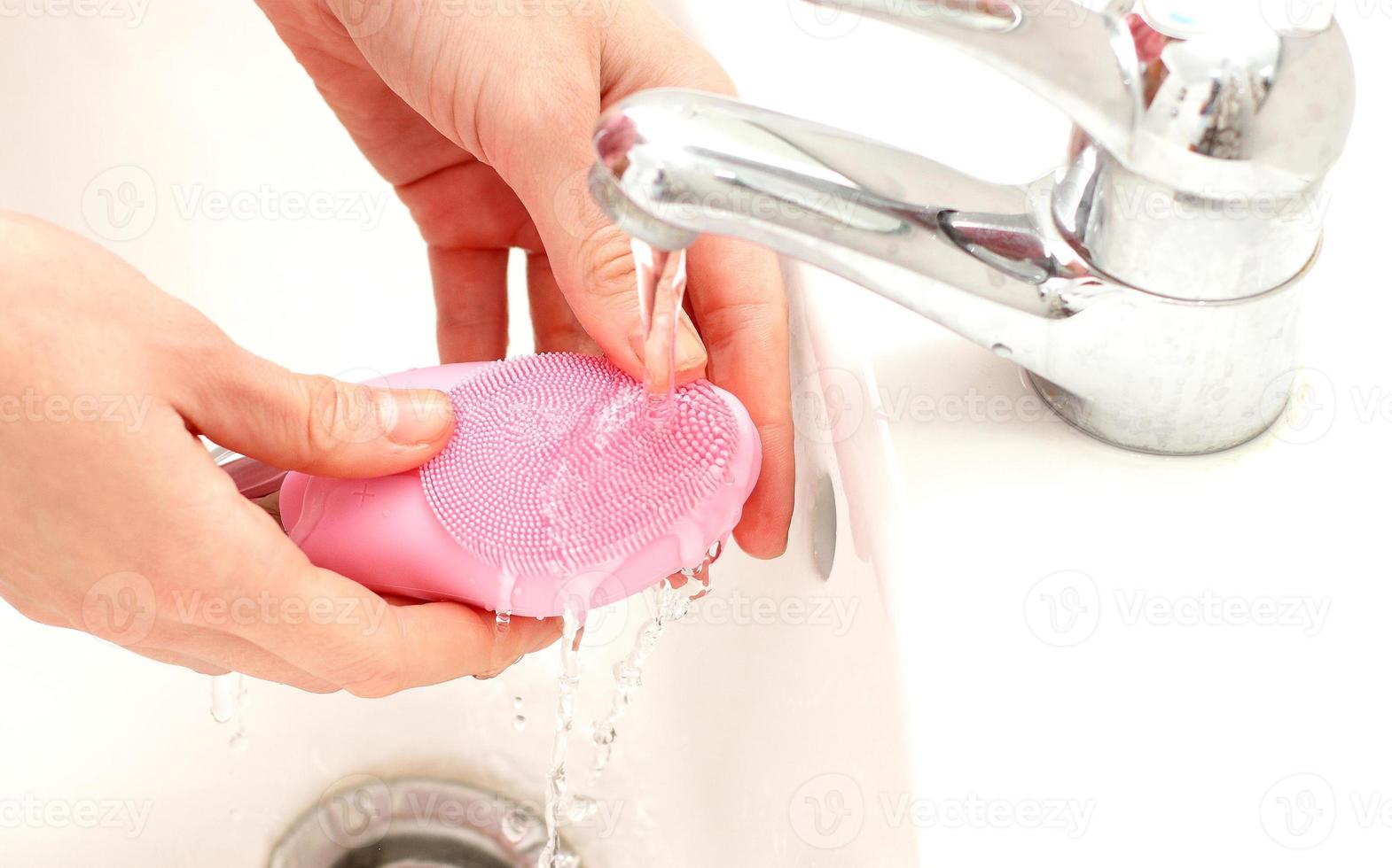 escova sônica de limpeza facial sob a água no banho, tratamento caseiro para a pele foto