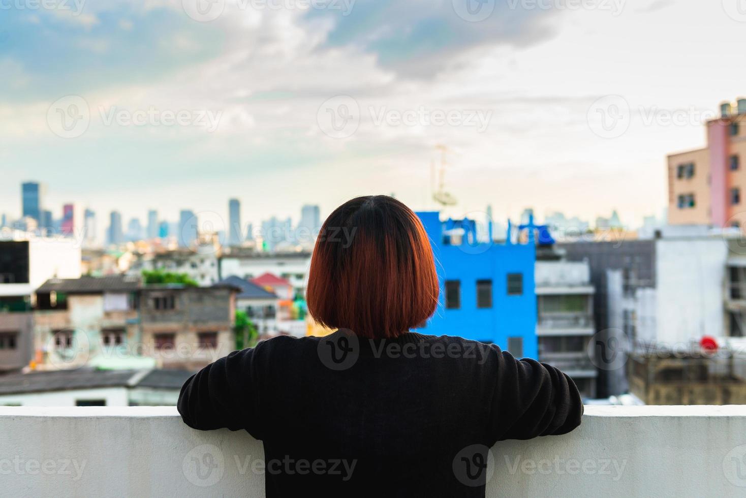 Mulher asiática sozinha sentada no telhado de um prédio ver a vista da cidade no pôr do sol da noite. foto