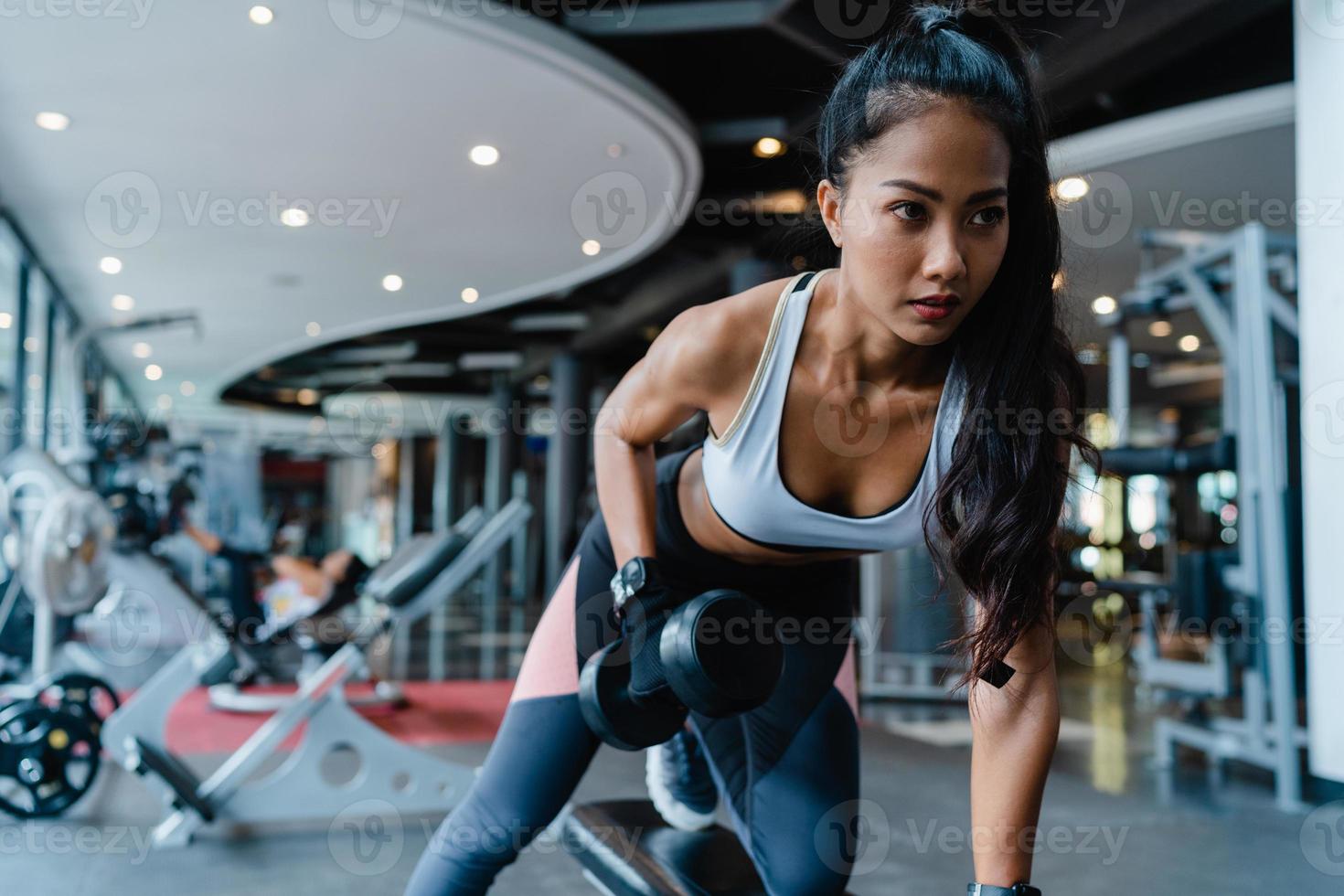 bela jovem asiática exercício fazendo levantamento de peso na barra de exercícios de queima de gordura na aula de fitness. atleta com tanquinho, atividade recreativa de desportista, treinamento funcional, conceito de estilo de vida saudável. foto