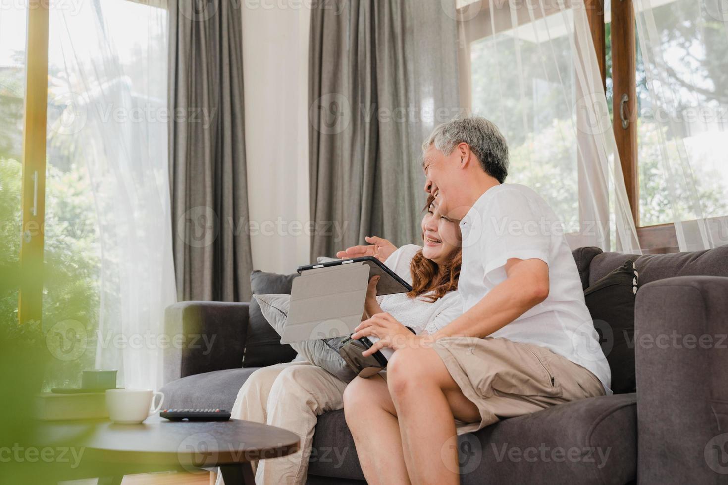 casal de idosos asiáticos usando tablet e simulador de realidade virtual jogando jogos na sala de estar, casal se sentindo feliz usando o tempo juntos, deitados no sofá em casa. família sênior do estilo de vida no conceito de casa. foto