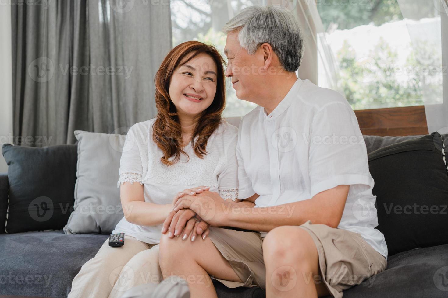 casal sênior asiático relaxa em casa. avós chineses sênior asiáticos, marido e mulher sorriso feliz abraço conversando enquanto estava deitado no sofá na sala de estar em casa conceito. foto