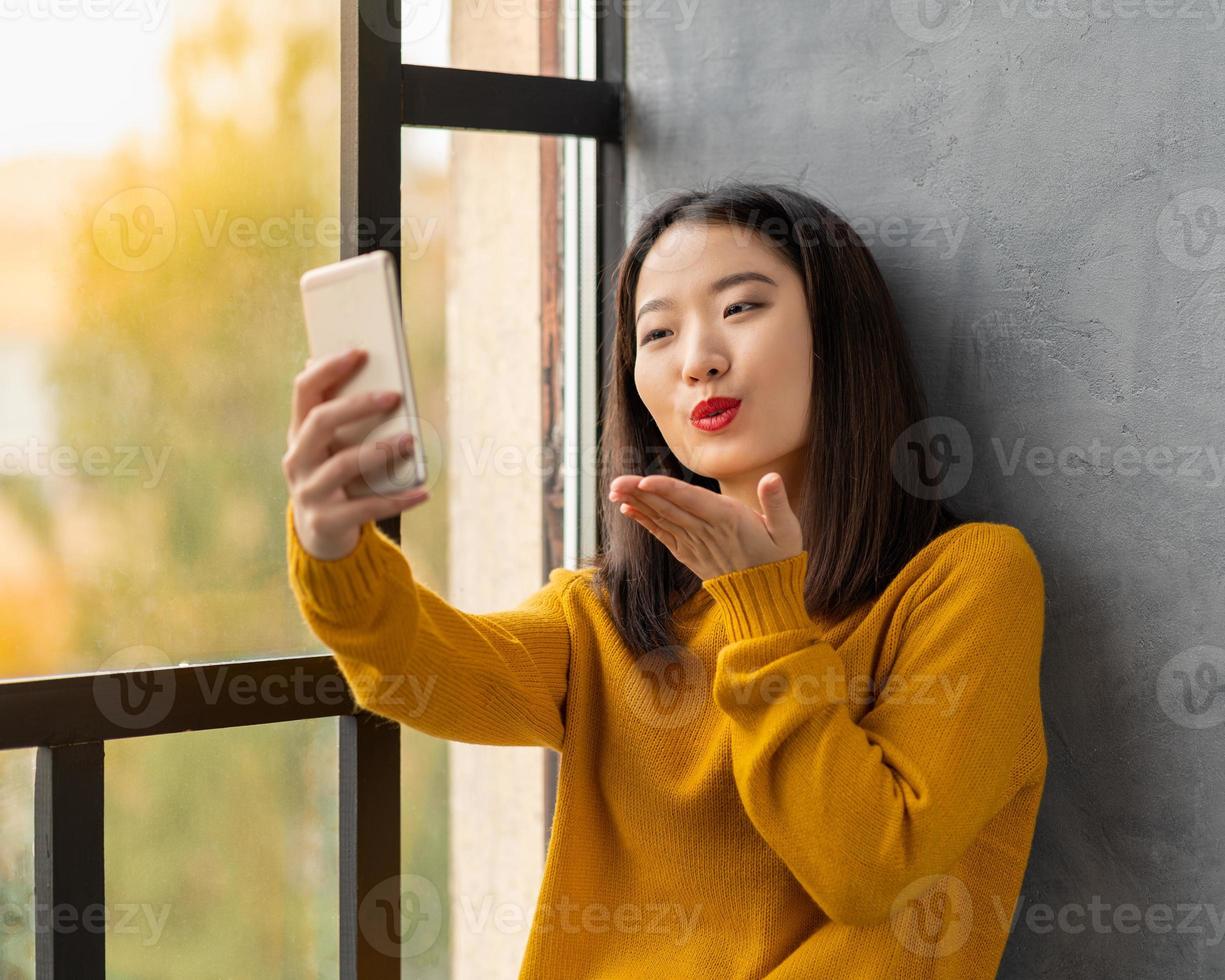 jovem mulher asiática tomando selfie e mandando beijo. linda adolescente foto