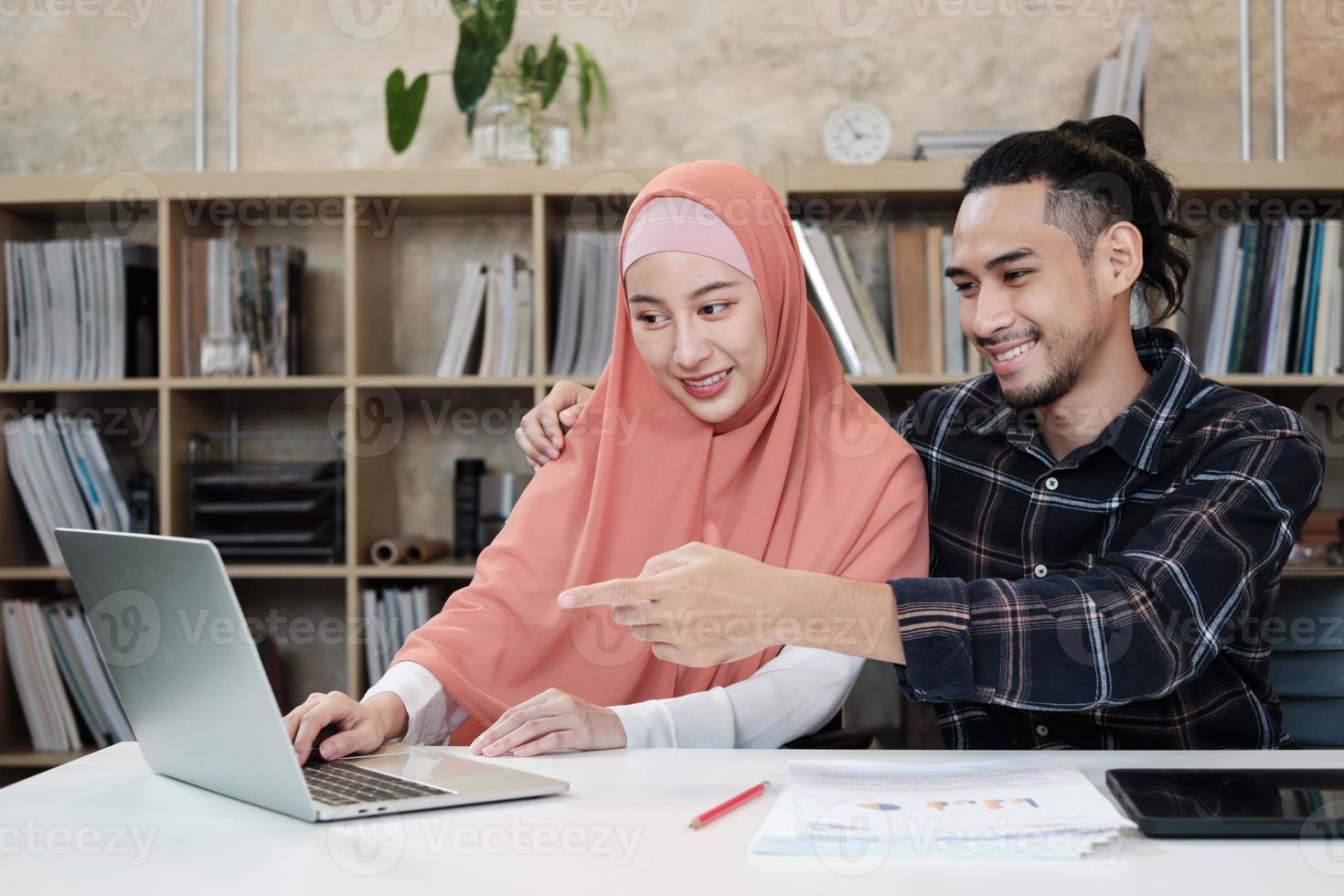 dois jovens colegas de inicialização que são casais islâmicos falam com um sorriso sobre o sucesso de trabalhar em um negócio de comércio eletrônico. use o laptop para comunicação on-line pela Internet em um pequeno escritório. foto