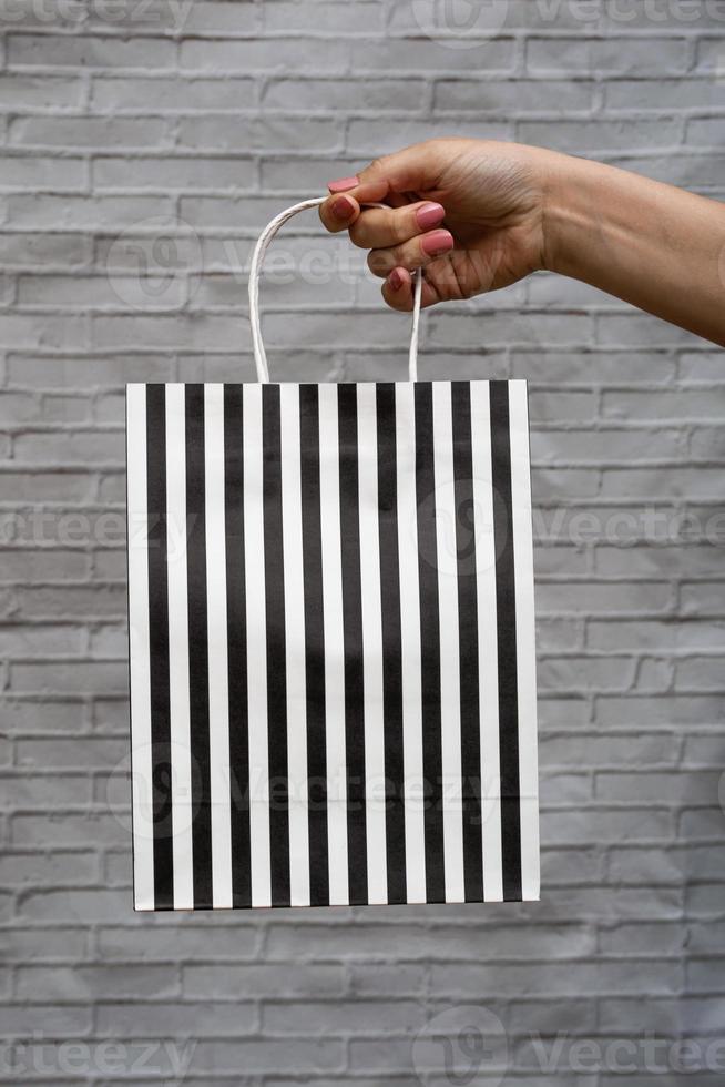 maquete de close-up de embalagem ecológica em um fundo cinza de tijolo. bolsa kraft em listras pretas e brancas na mão de uma mulher. compras online foto