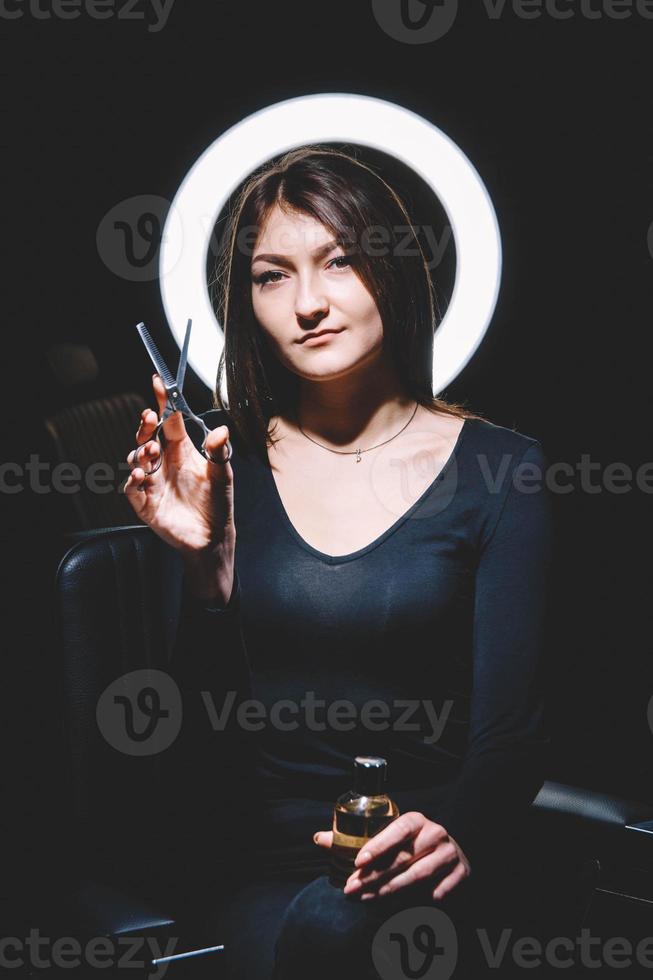cabeleireira linda com uma tesoura na mão em um fundo preto foto