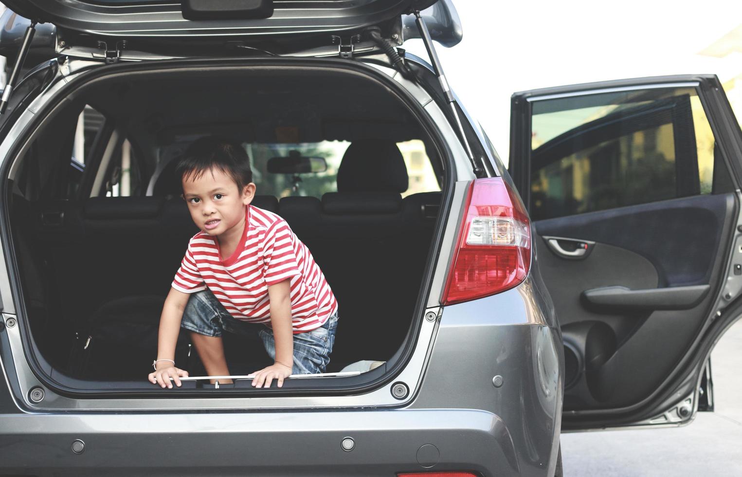 um menino brincando de safado no porta-malas de um carro foto