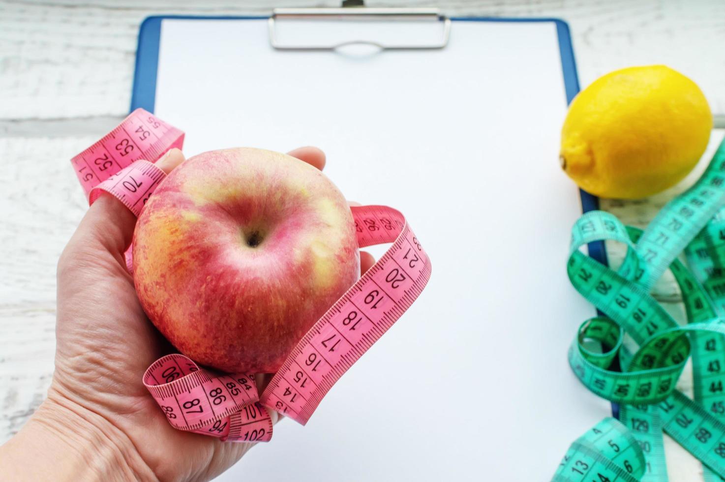 uma maçã vermelha e uma fita de um centímetro nas mãos de uma mulher no fundo de um caderno. dieta, corpo saudável, nutrição adequada. foto