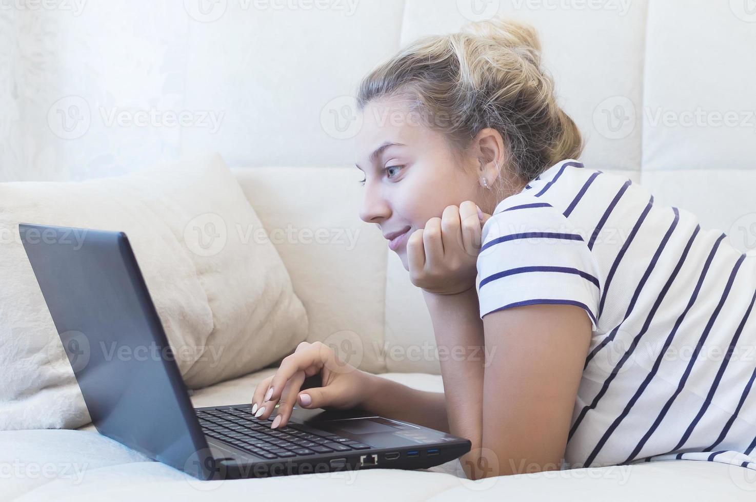 loira está sentada em casa no sofá com um laptop e se comunica na internet. redes sociais. namorando. foto
