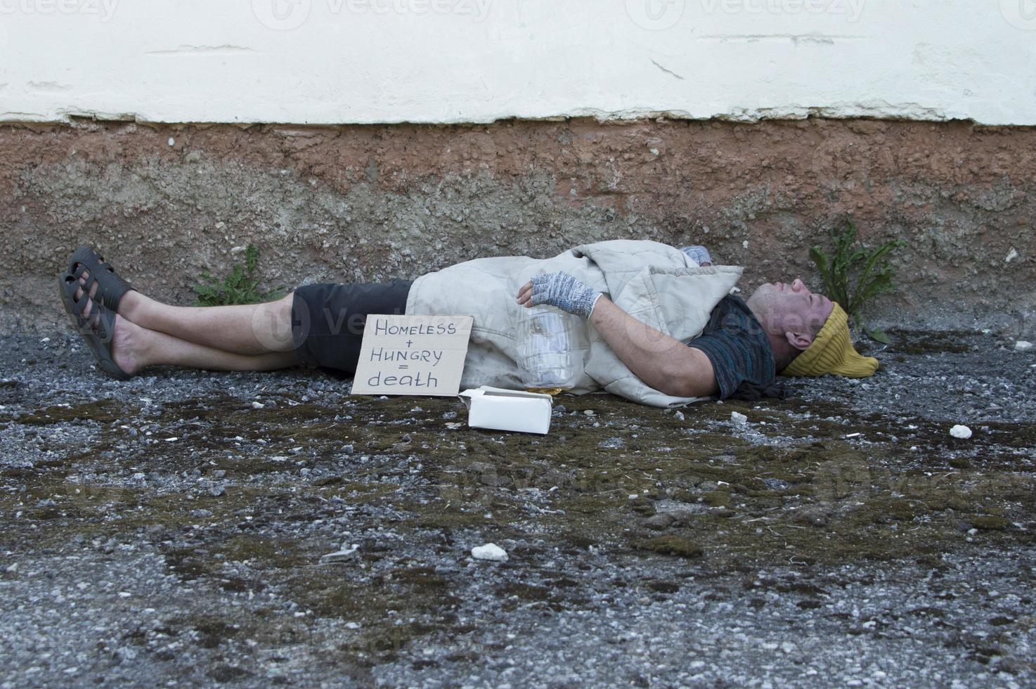 um mendigo embriagado dorme na rua com uma garrafa de cerveja nas mãos. pobreza, desemprego, alcoolismo. foto