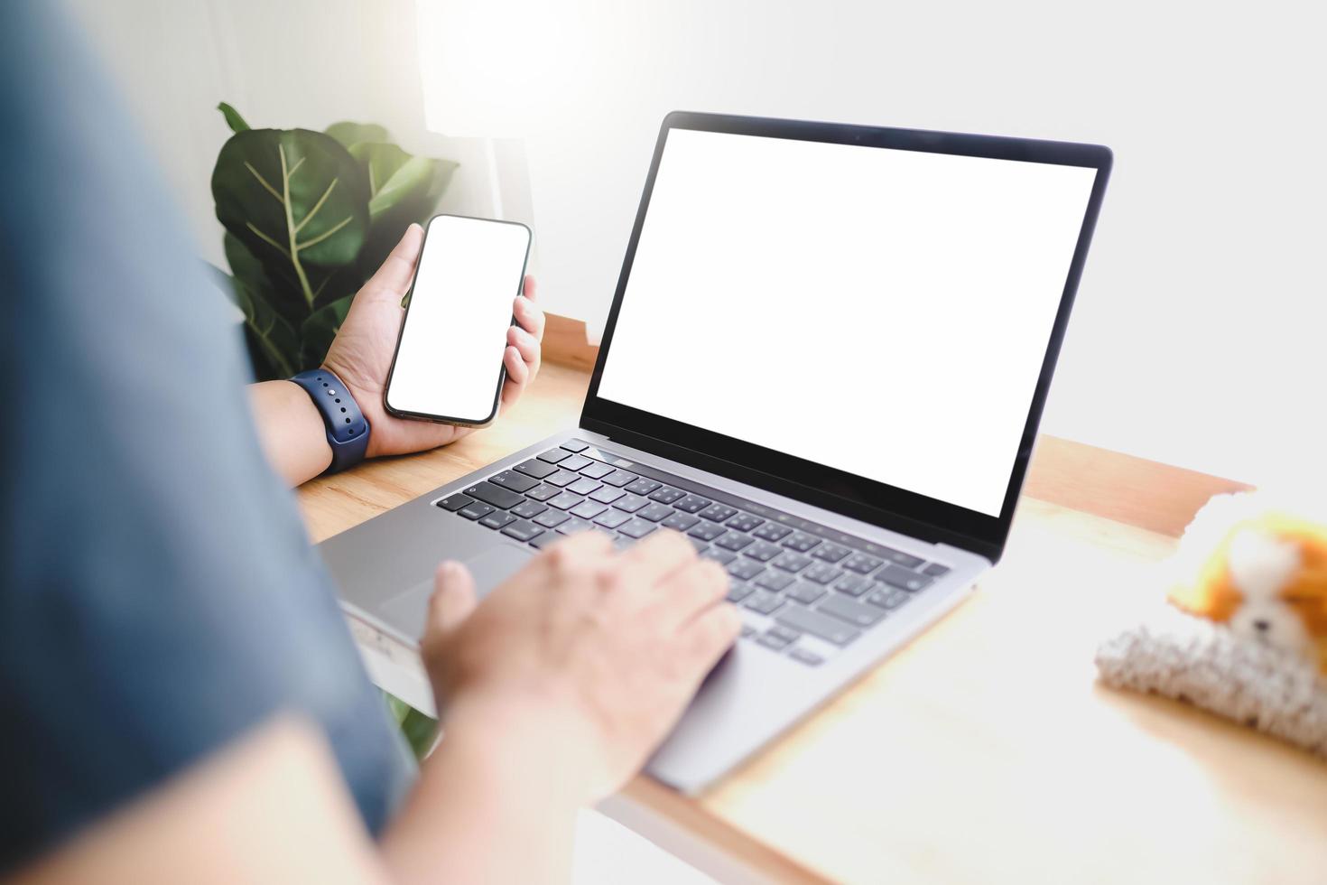 imagem de maquete das mãos do homem segurando um telefone celular branco e laptop com tela em branco na coxa e uma xícara de café no café foto