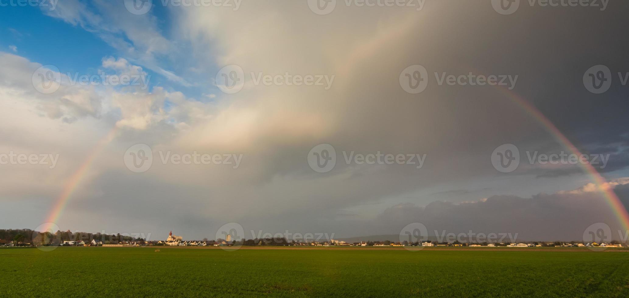 maravilhoso grande arco-íris com um campo verde de vila e um maravilhoso panorama do céu foto
