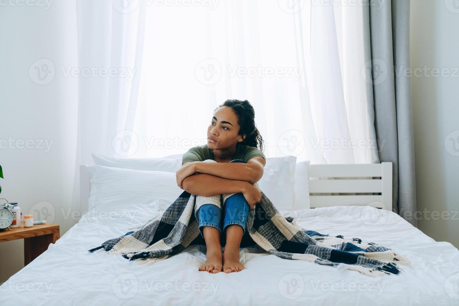 mulher afro-americana triste enrolada em um cobertor e olhando para o lado foto