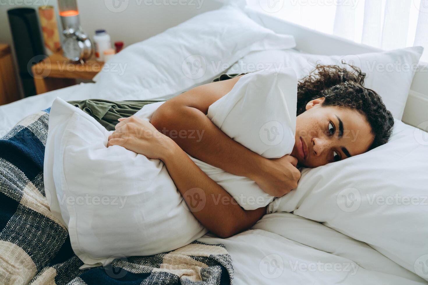 mulher africana sem emoção, enrolada em um cobertor e abraçando o travesseiro foto