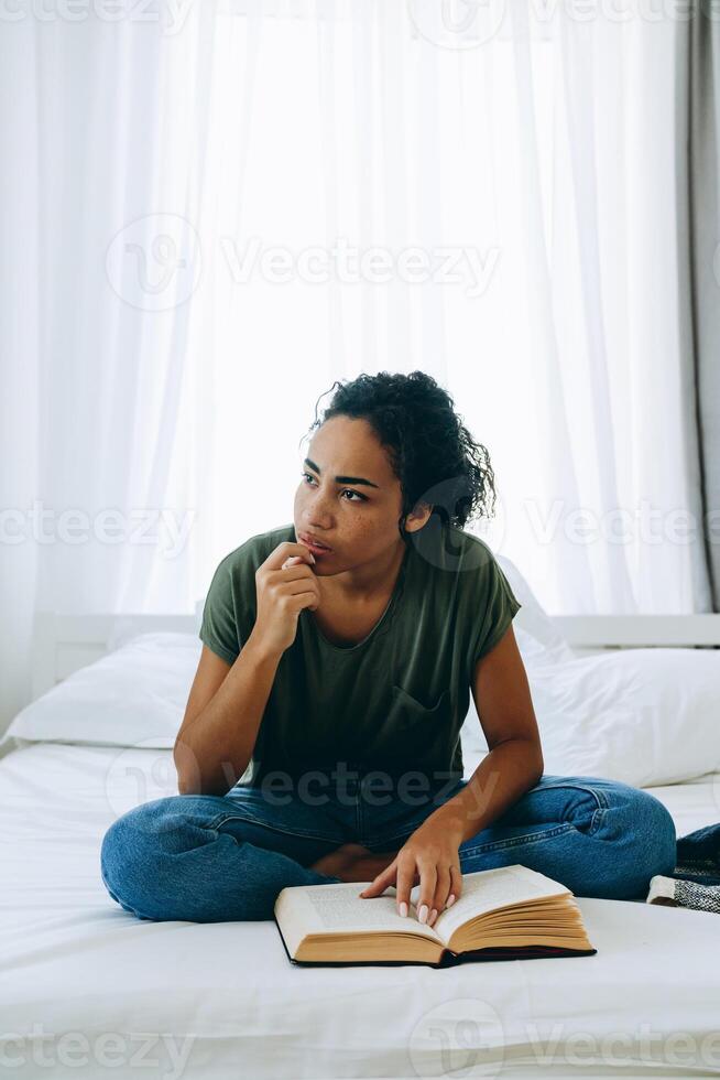 mulher africana pensativa lendo livro e olhando para o lado foto