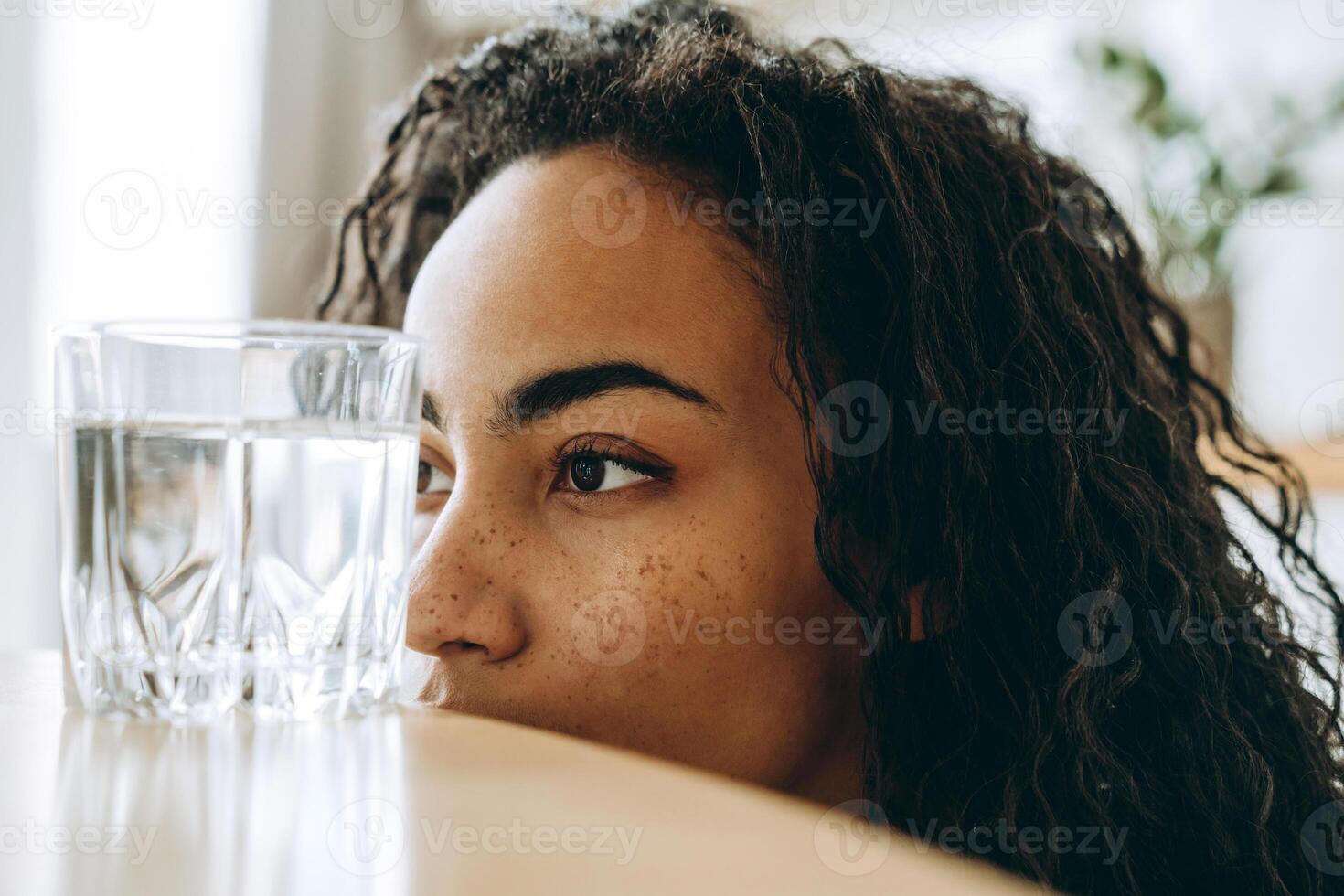 jovem negra olhando para um copo de água enquanto está sentada na cozinha foto