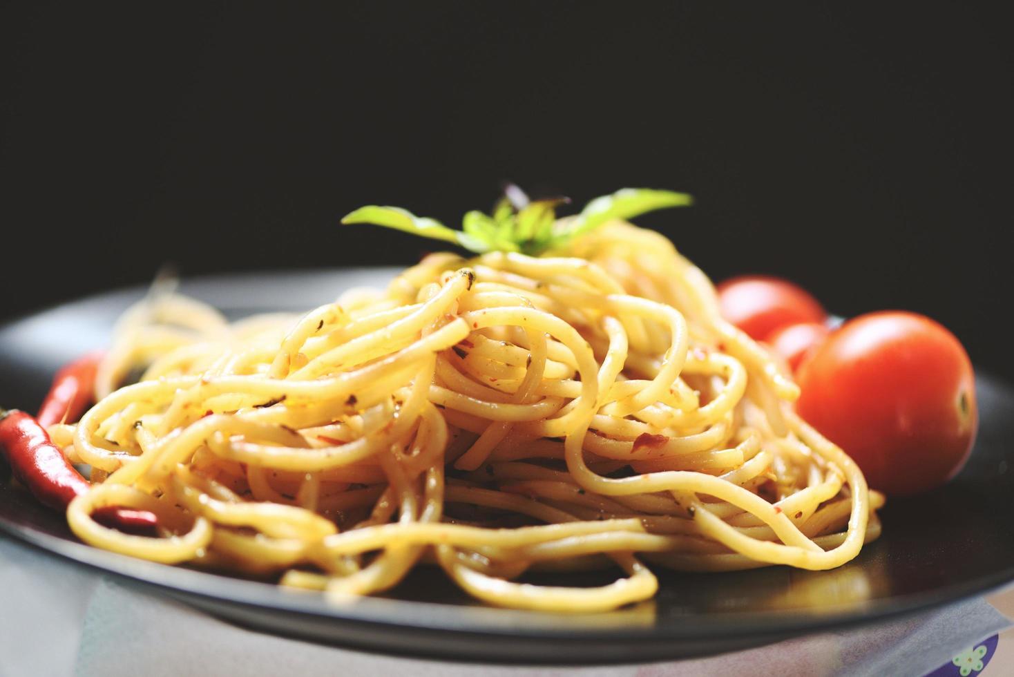 macarrão espaguete e tomate pimenta e folhas de manjericão tradicional deliciosa comida italiana espaguete à bolonhesa no prato na mesa de jantar com preto foto