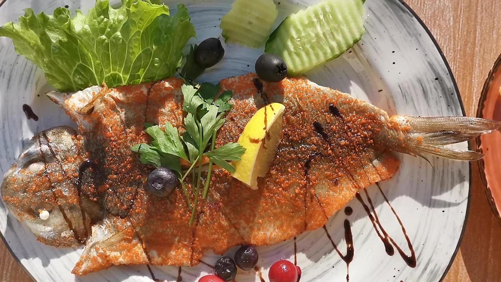 peixe frito em um prato branco com limão e frutas vermelhas foto