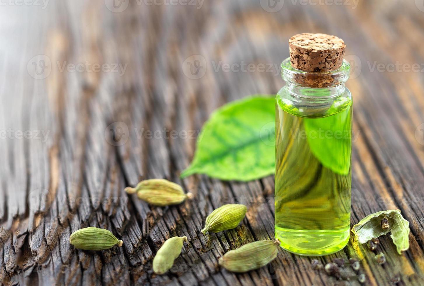 uma garrafa de óleo essencial de cardamomo com sementes de cardamomo e folhas em um fundo de madeira foto