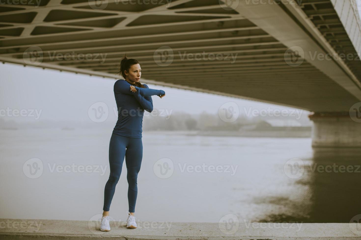 jovem de macacão azul alongando-se antes do treino à beira do rio na manhã de outono foto