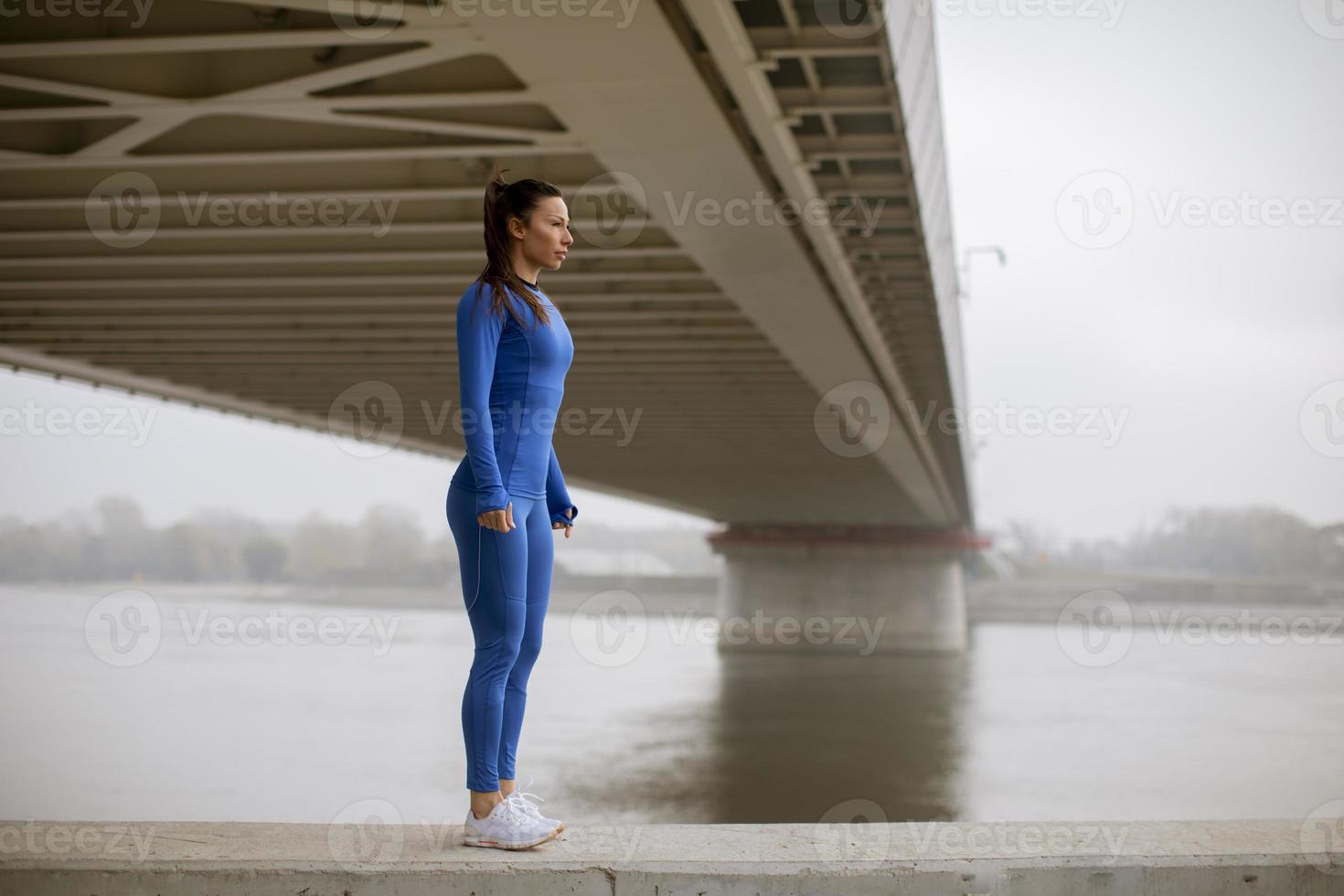 jovem de macacão azul alongando-se antes do treino à beira do rio na manhã de outono foto