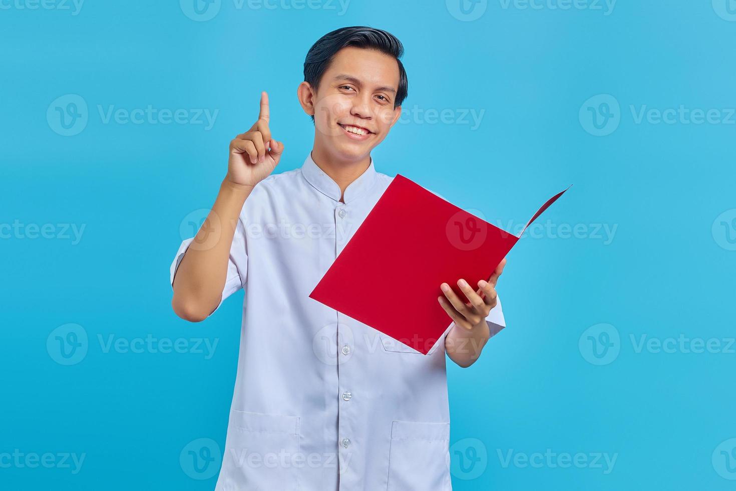 retrato de alegre enfermeira segurando uma pasta em pé e apontando para cima sobre um fundo azul foto