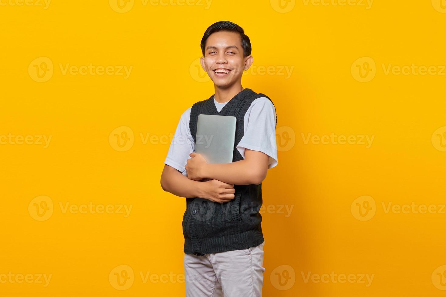 retrato de homem asiático alegre trazendo laptop sobre fundo amarelo foto