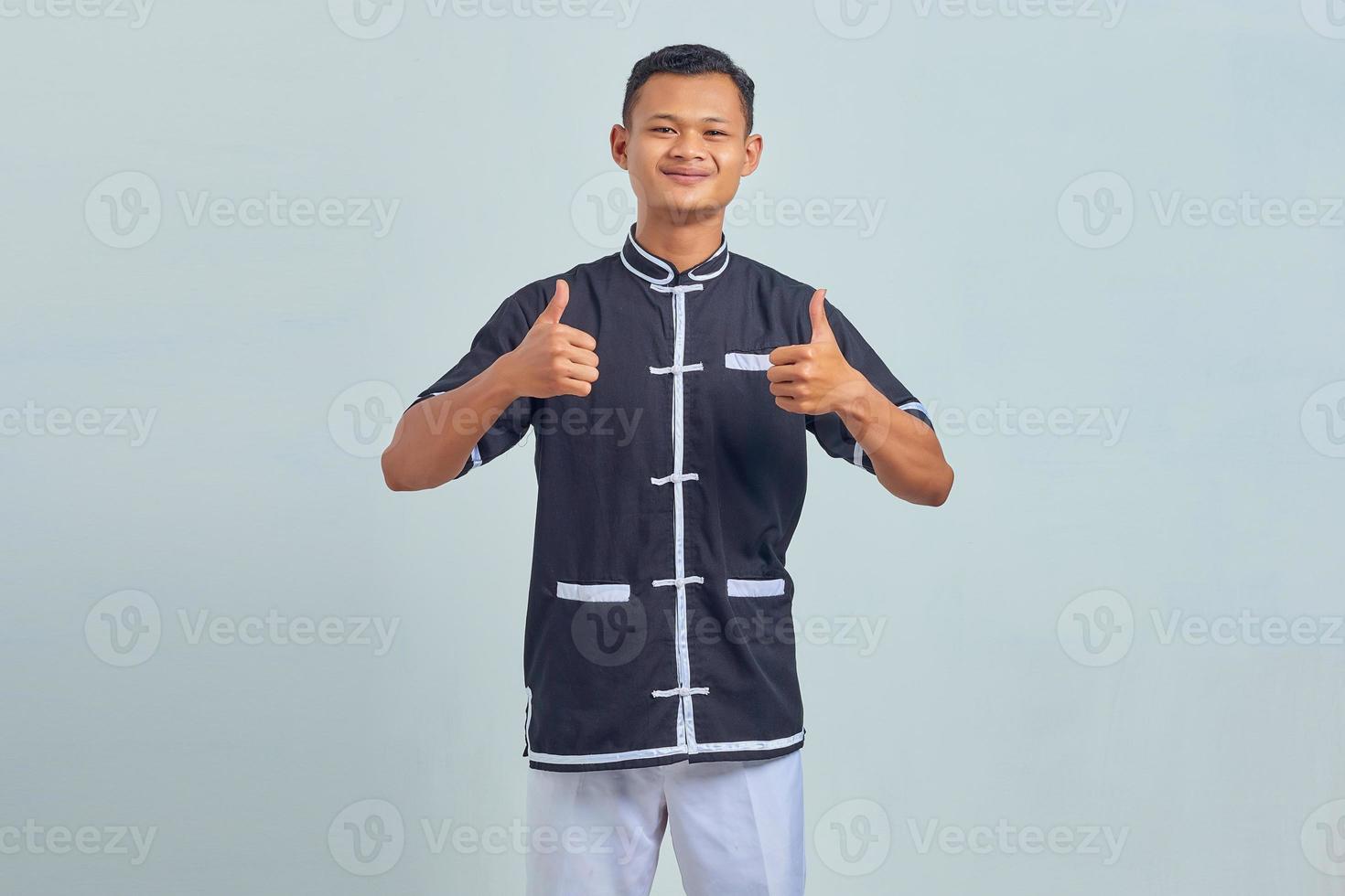 retrato de um jovem asiático sorridente usando caratê mostrando os polegares para cima ou um sinal de aprovação sobre um fundo cinza foto