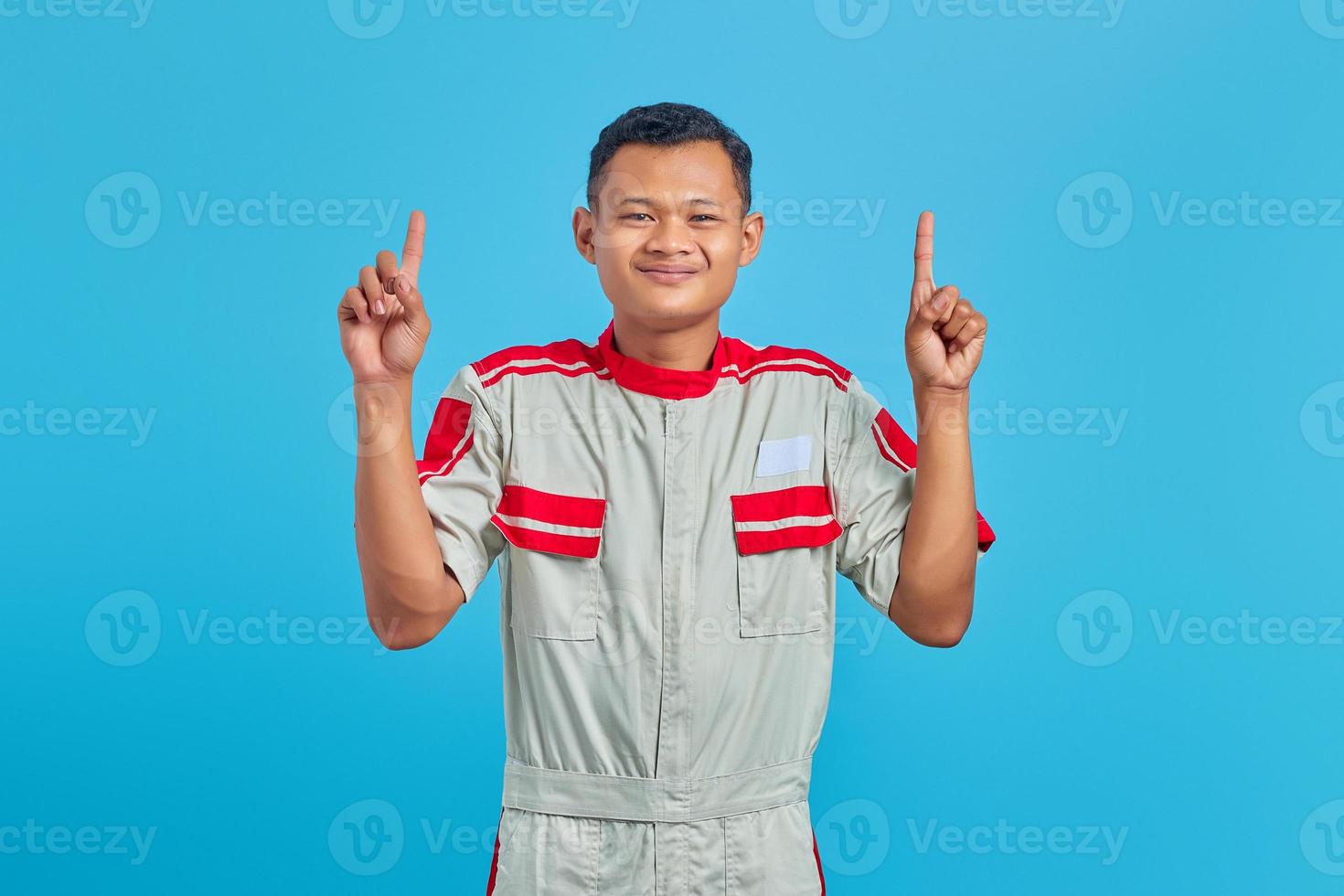 retrato de um jovem mecânico asiático sorridente enquanto levanta o dedo isolado sobre fundo azul foto