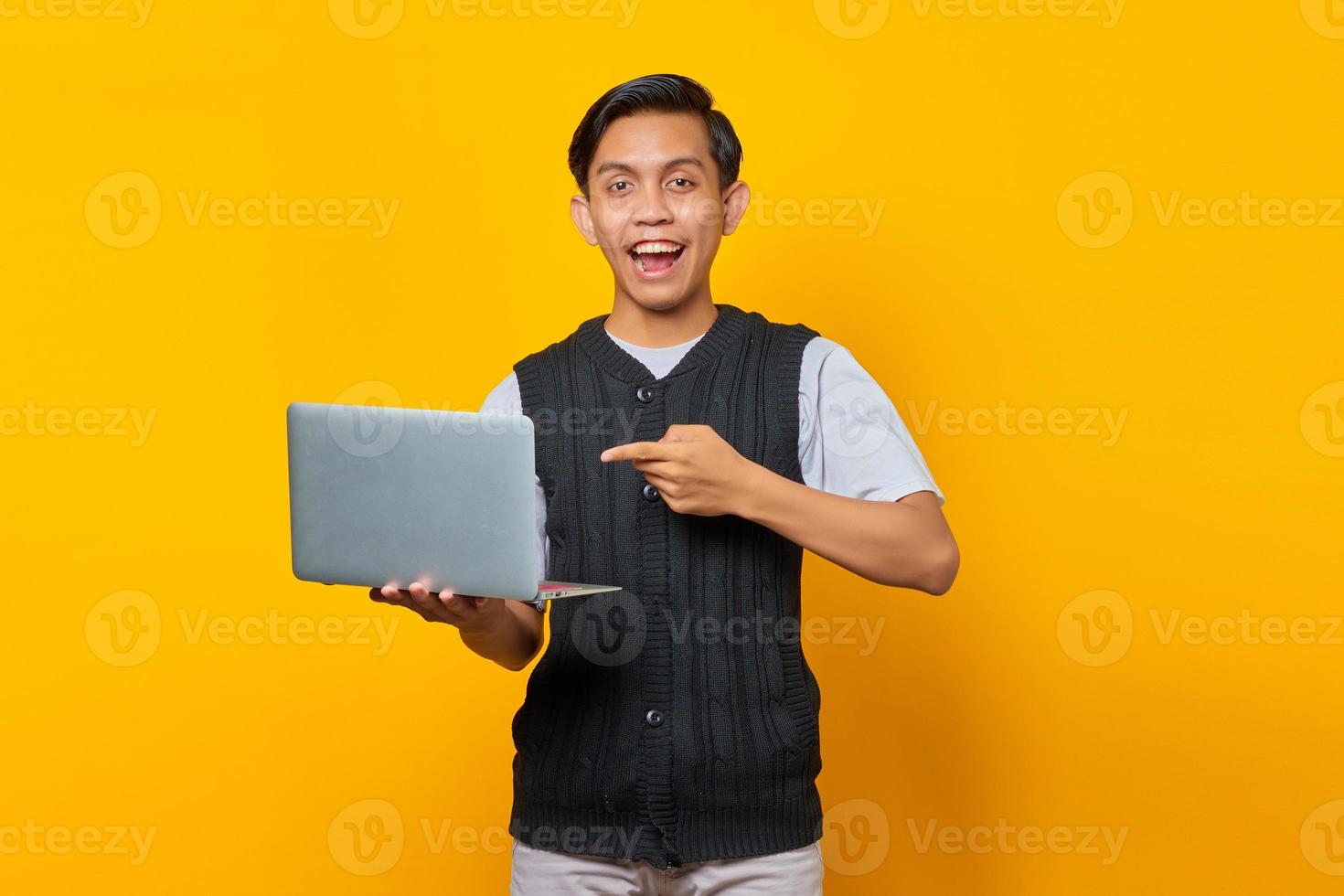jovem bonito animado apontando para um laptop sobre fundo amarelo foto
