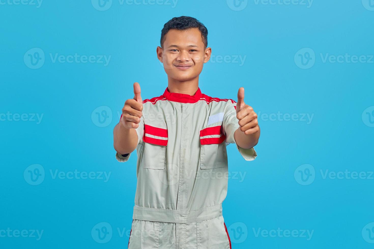 retrato de um jovem mecânico asiático sorridente, mostrando o polegar para cima gesto isolado sobre fundo azul foto