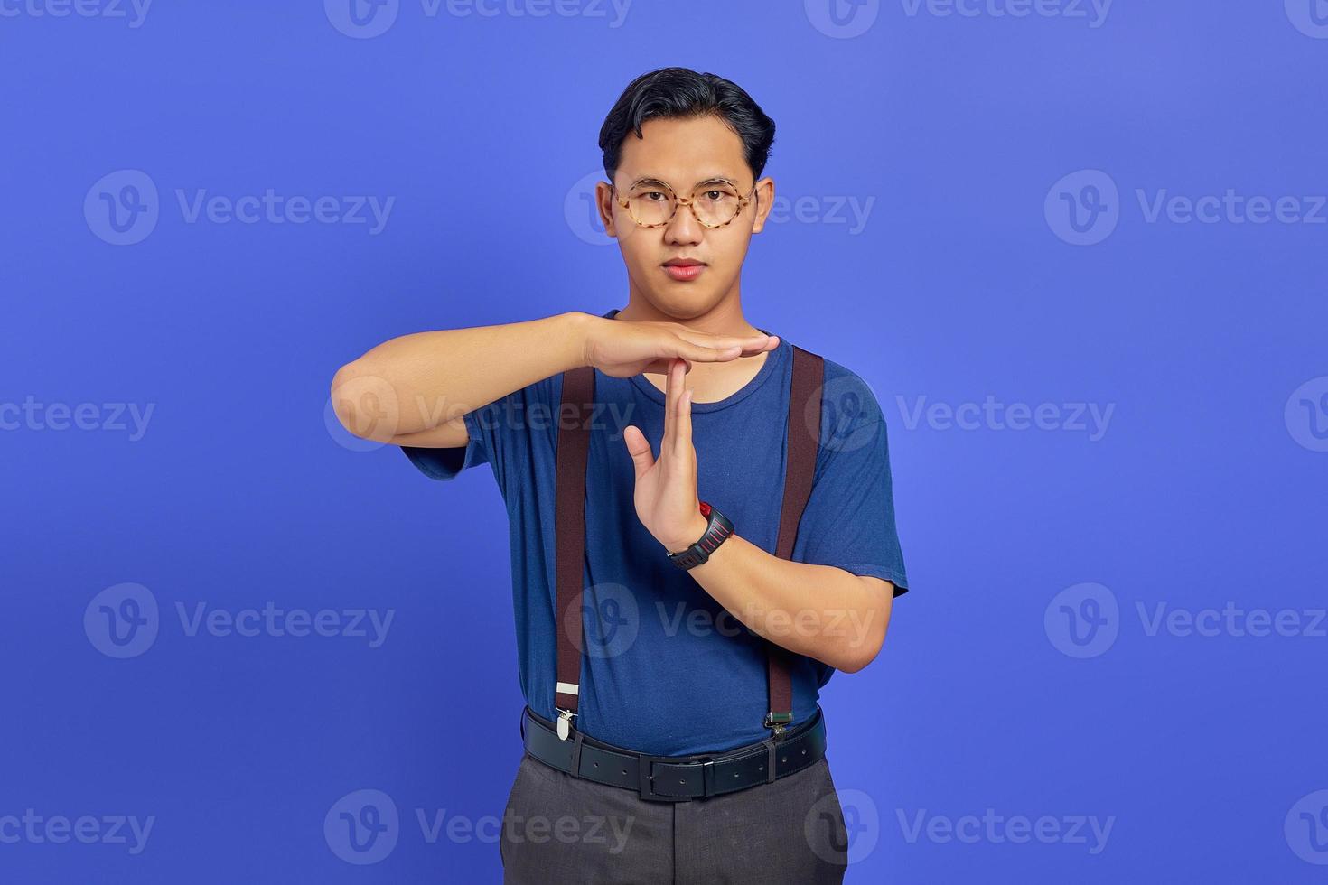 homem vestindo camisa azul e óculos, mostrando gesto de tempo limite em fundo roxo foto