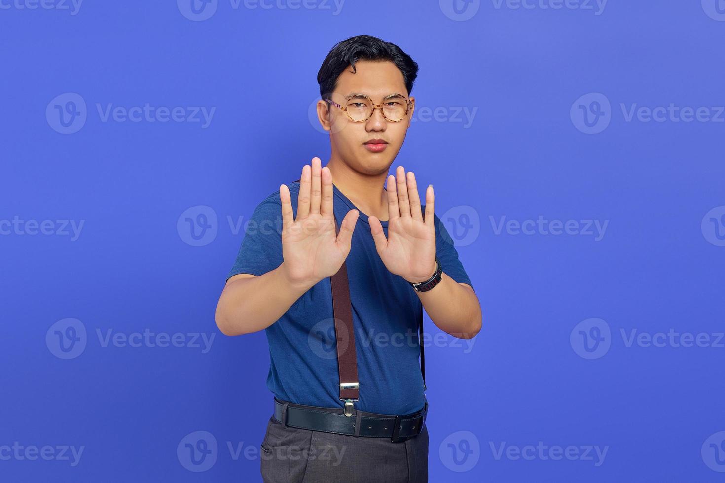 retrato de homem bonito bravo fazendo gesto de parada com as palmas das mãos no fundo roxo foto