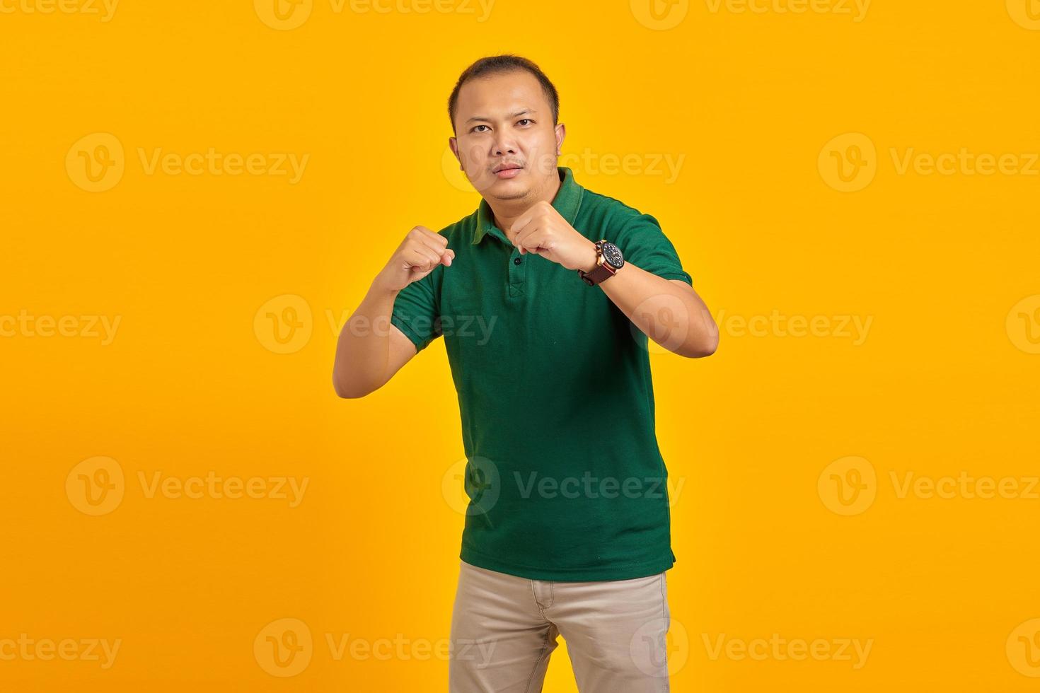 retrato de homem asiático jovem com raiva mostrando gesto de boxeador em fundo amarelo foto