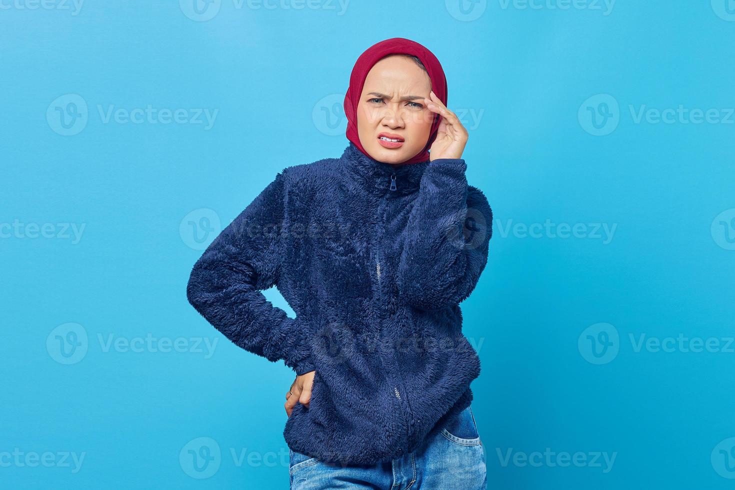 retrato de uma jovem mulher asiática parecendo tonta e com dor de cabeça em fundo azul foto