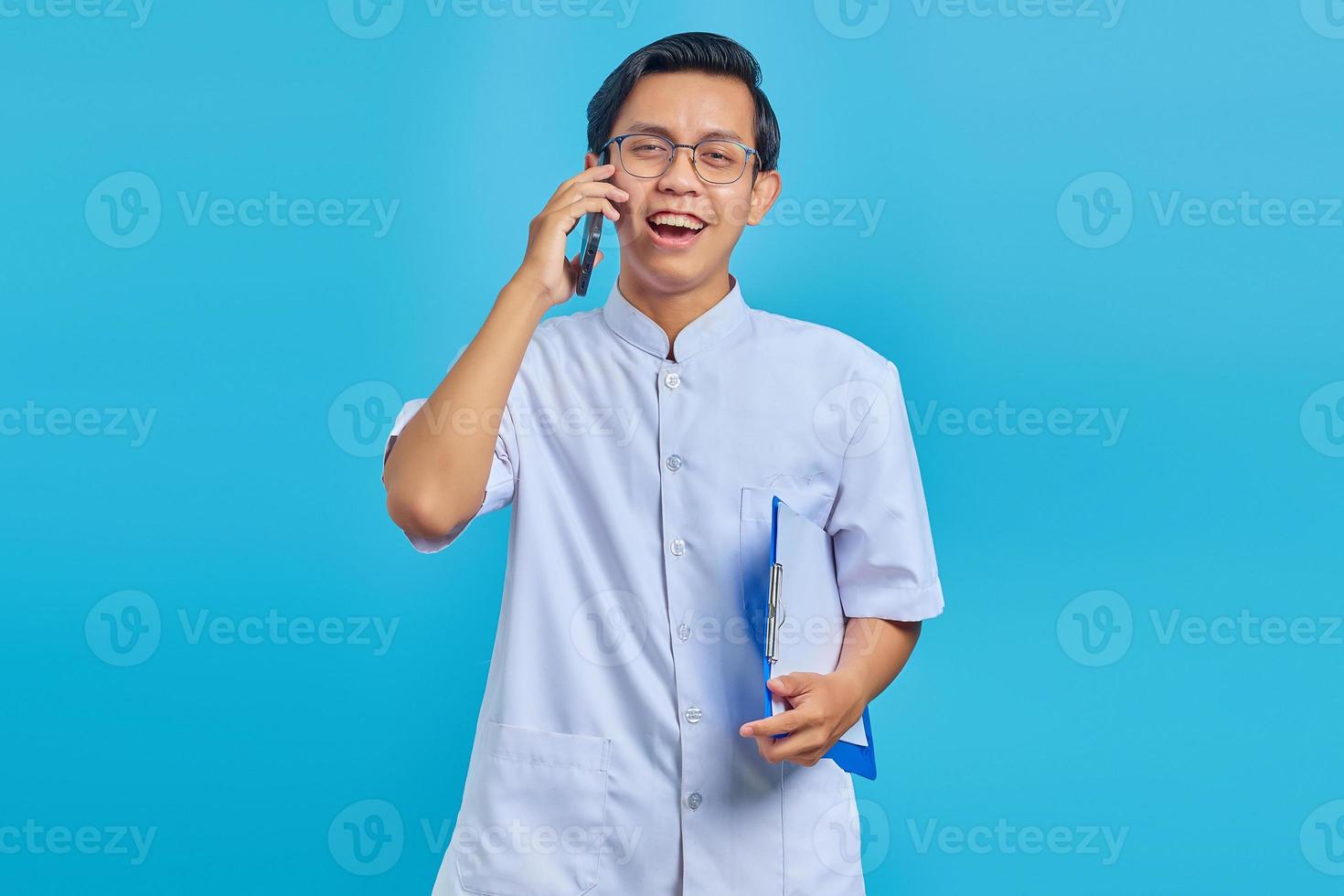 alegre bonito enfermeiro segurando uma prancheta e falando no celular sobre fundo amarelo foto