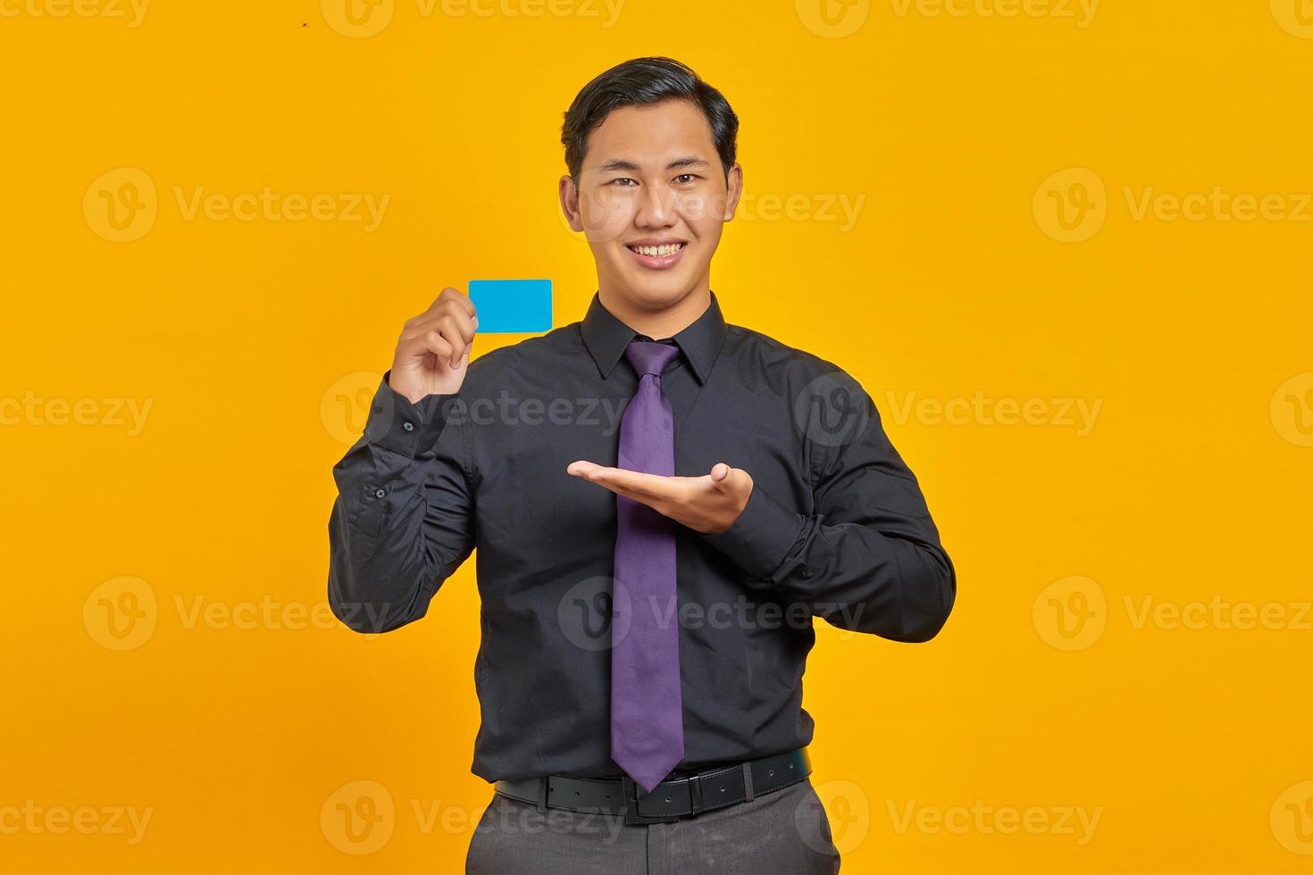 alegre empresário asiático mostrando cartão de crédito sobre fundo amarelo foto