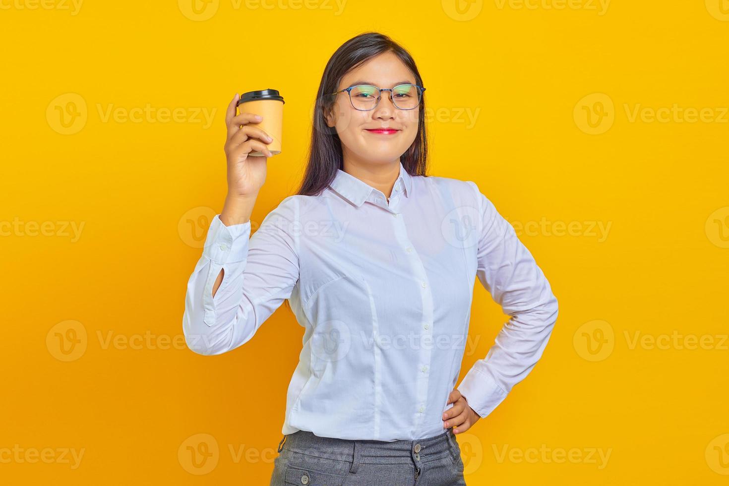 foto de mulher de negócios asiática sorridente e alegre, vestindo uma camisa branca, segurando uma xícara de café recém-comprada sobre fundo amarelo