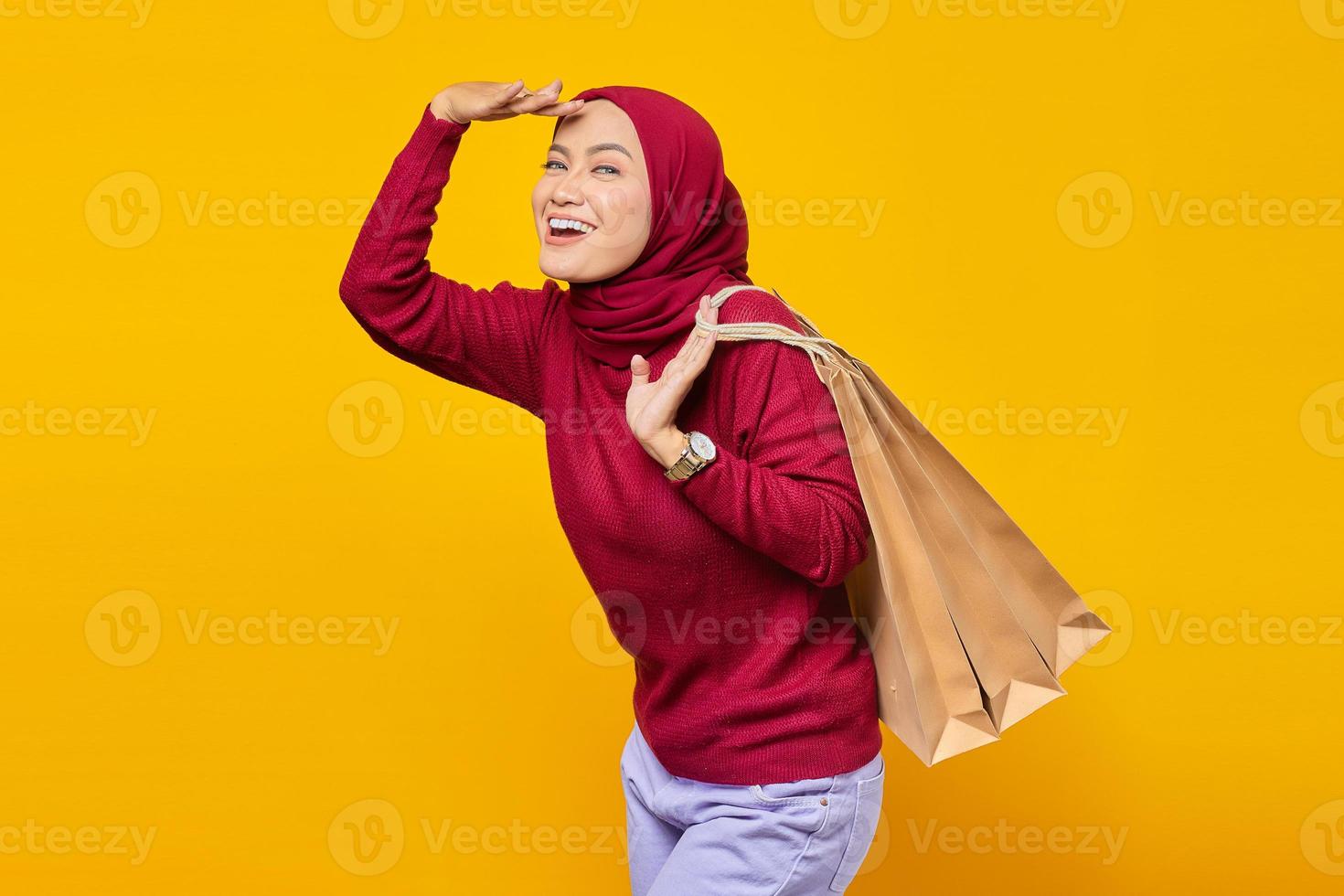 mulher asiática jovem e alegre, animada e segurando sacolas de compras no fundo amarelo foto