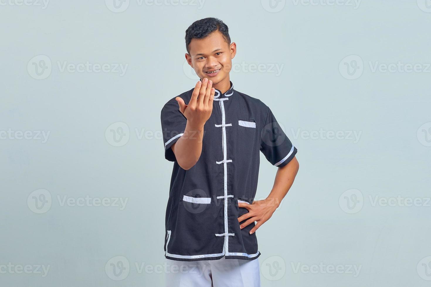 retrato de jovem asiático vestindo quimono taekwondo fazendo gesto convidativo com as palmas das mãos isoladas em um fundo cinza foto