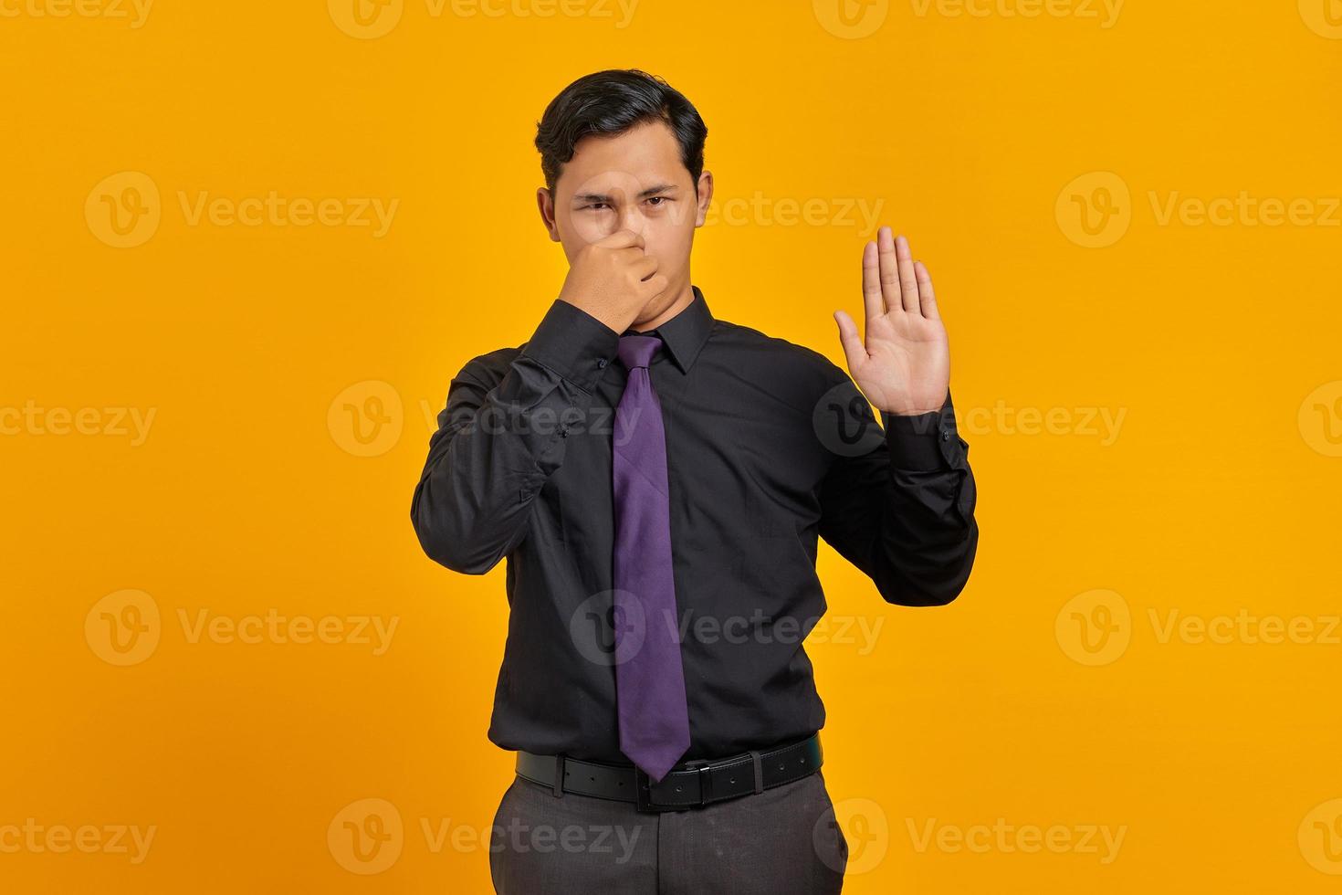 retrato de jovem empresário asiático segurando o nariz devido ao mau cheiro em fundo amarelo foto