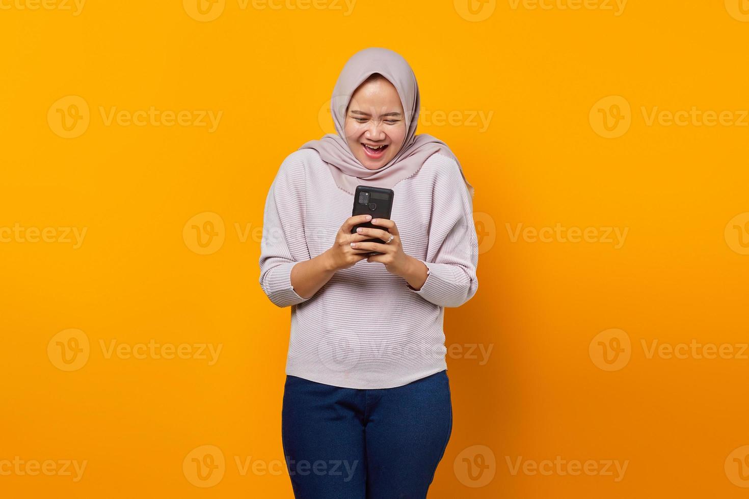 retrato de mulher asiática atraente e alegre usando telefone celular sobre fundo amarelo foto