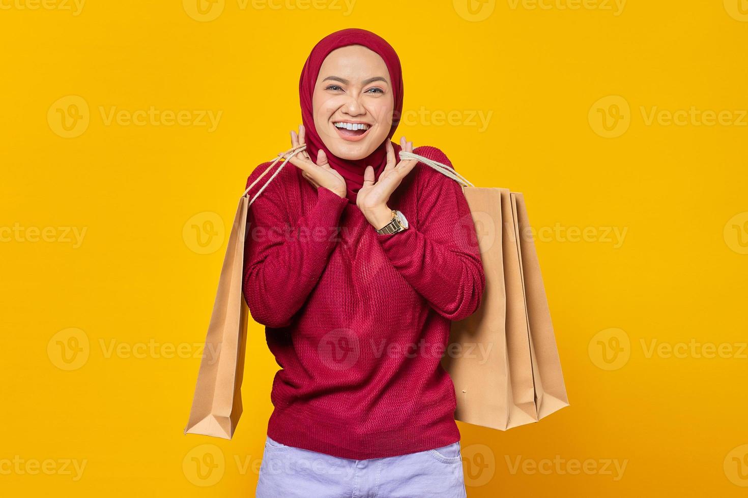 retrato de uma mulher asiática bonita e alegre segurando sacolas de compras em fundo amarelo foto