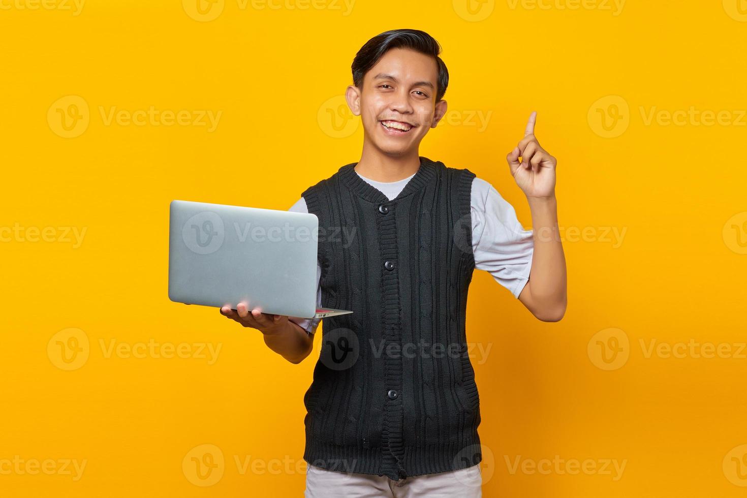 Feliz jovem bonito empresário tendo uma ideia criativa enquanto segura um laptop sobre fundo amarelo foto