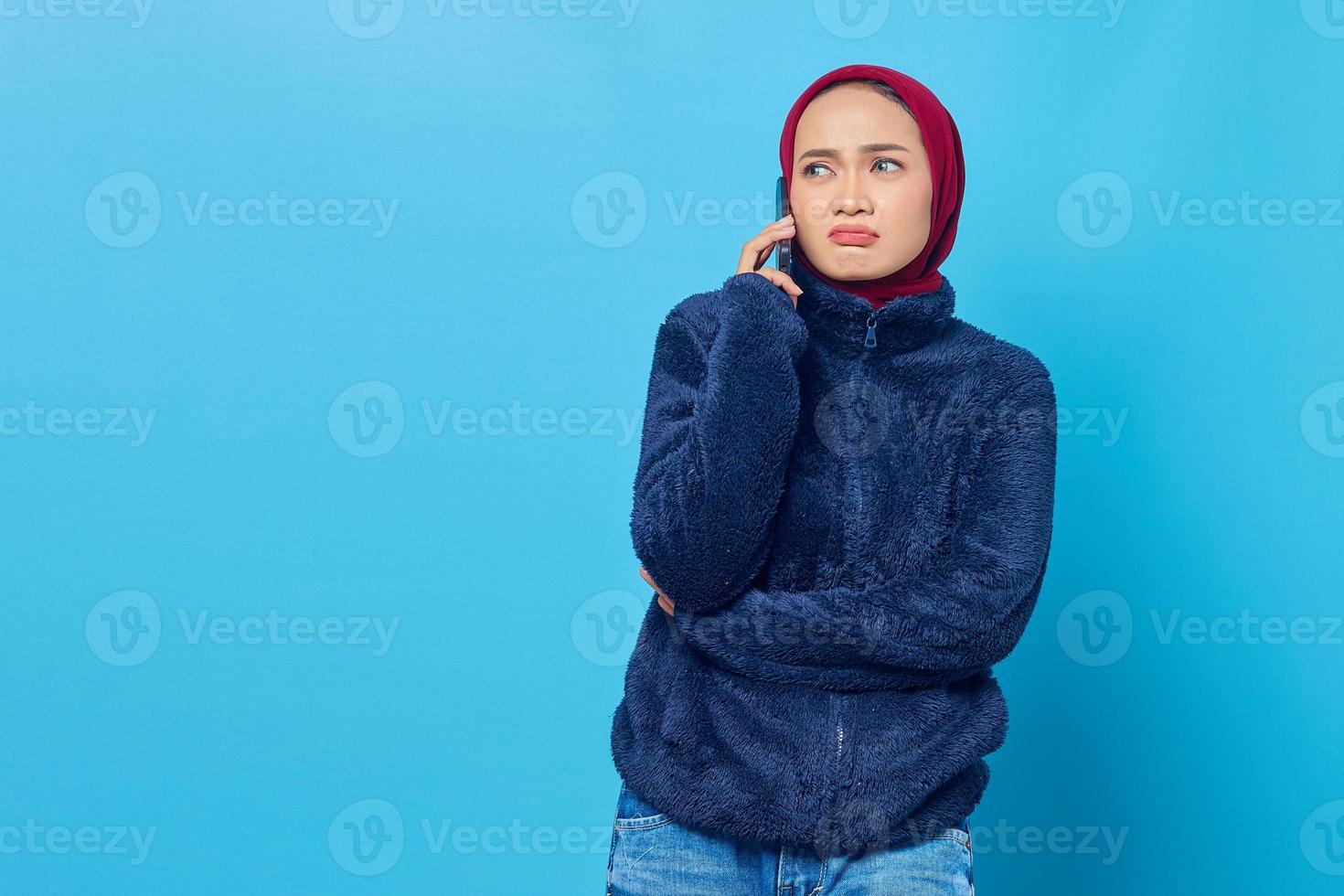 jovem asiática confusa falando em um telefone celular com o namorado, isolado em um fundo azul foto