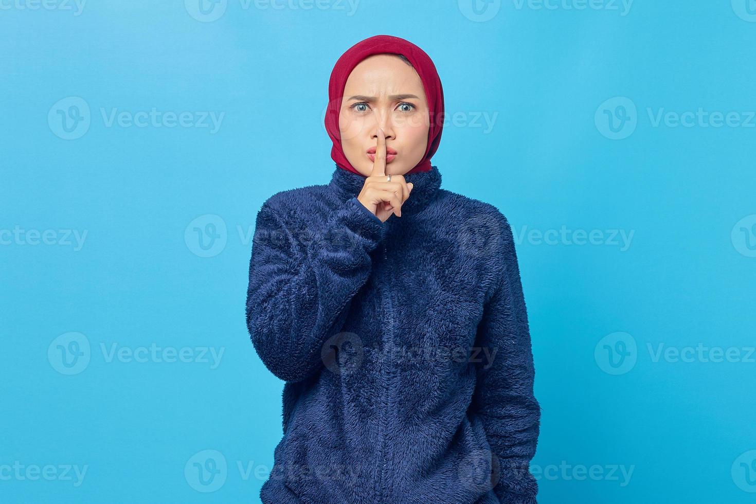 retrato de uma jovem mulher asiática atraente fazendo gesto de silêncio sobre fundo azul foto