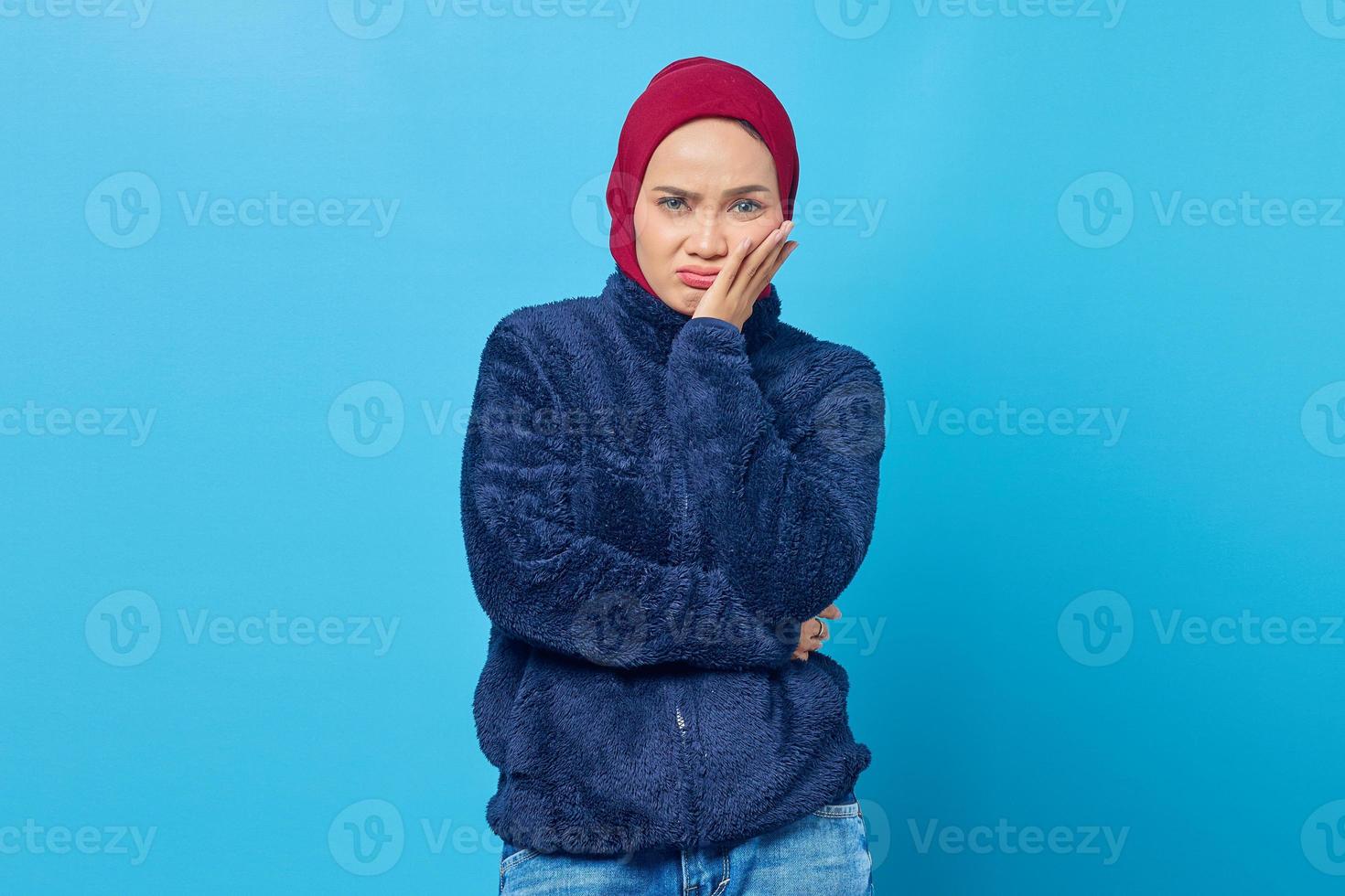 retrato de uma jovem asiática pensativa tocando o queixo com a mão e olhando para a câmera sobre fundo azul foto